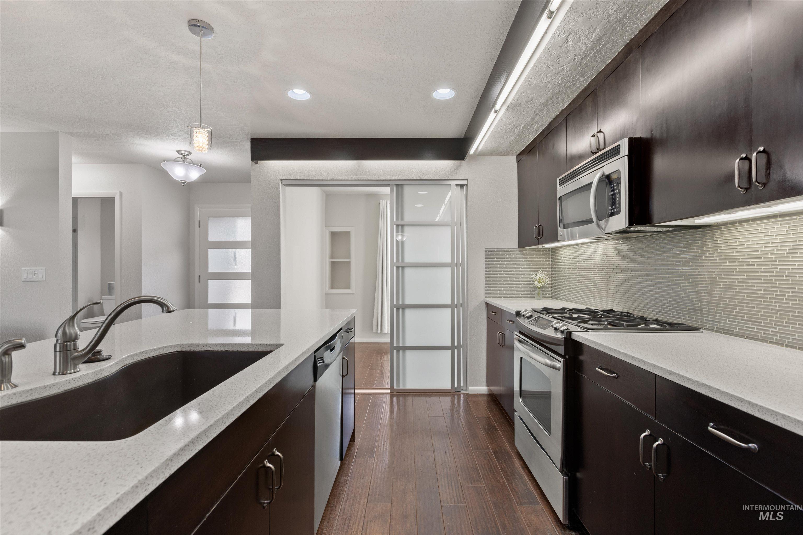 Kitchen with dark brown cabinetry, stainless steel appliances, pendant lighting, decorative backsplash, and a textured ceiling