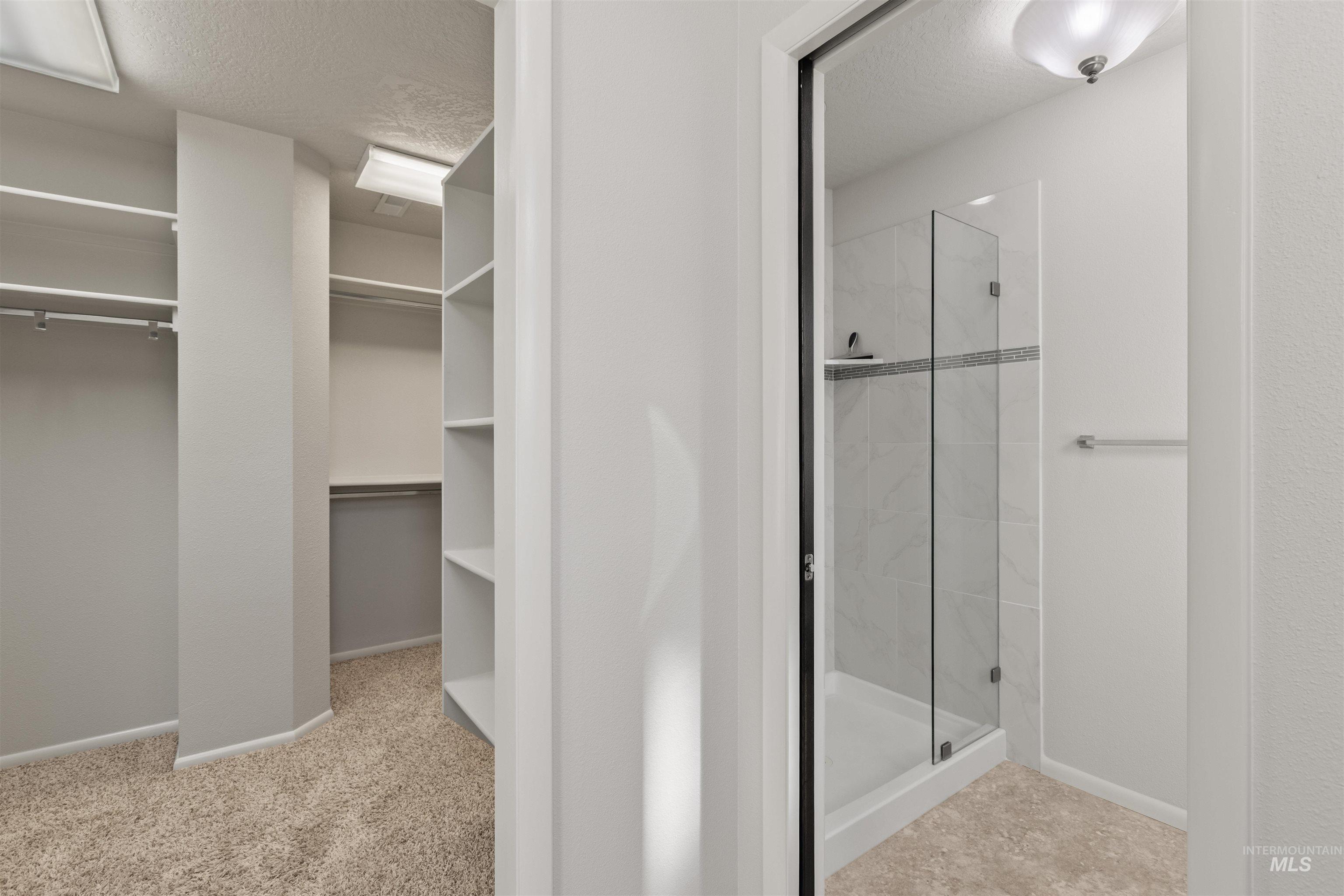 Full bath featuring a spacious closet, a textured ceiling, a shower stall, and light carpet