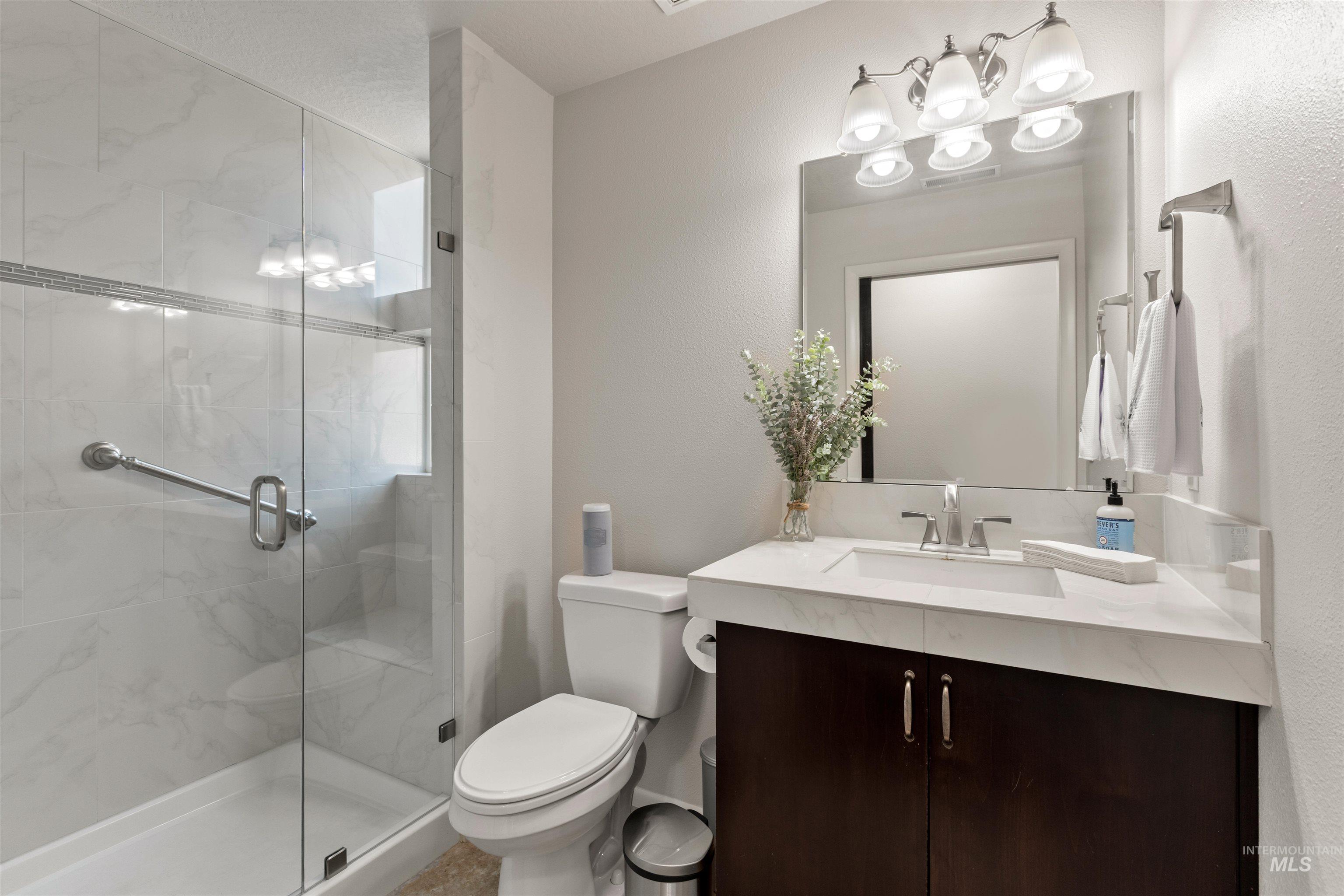 Full bath with vanity, a shower stall, a chandelier, and a textured wall