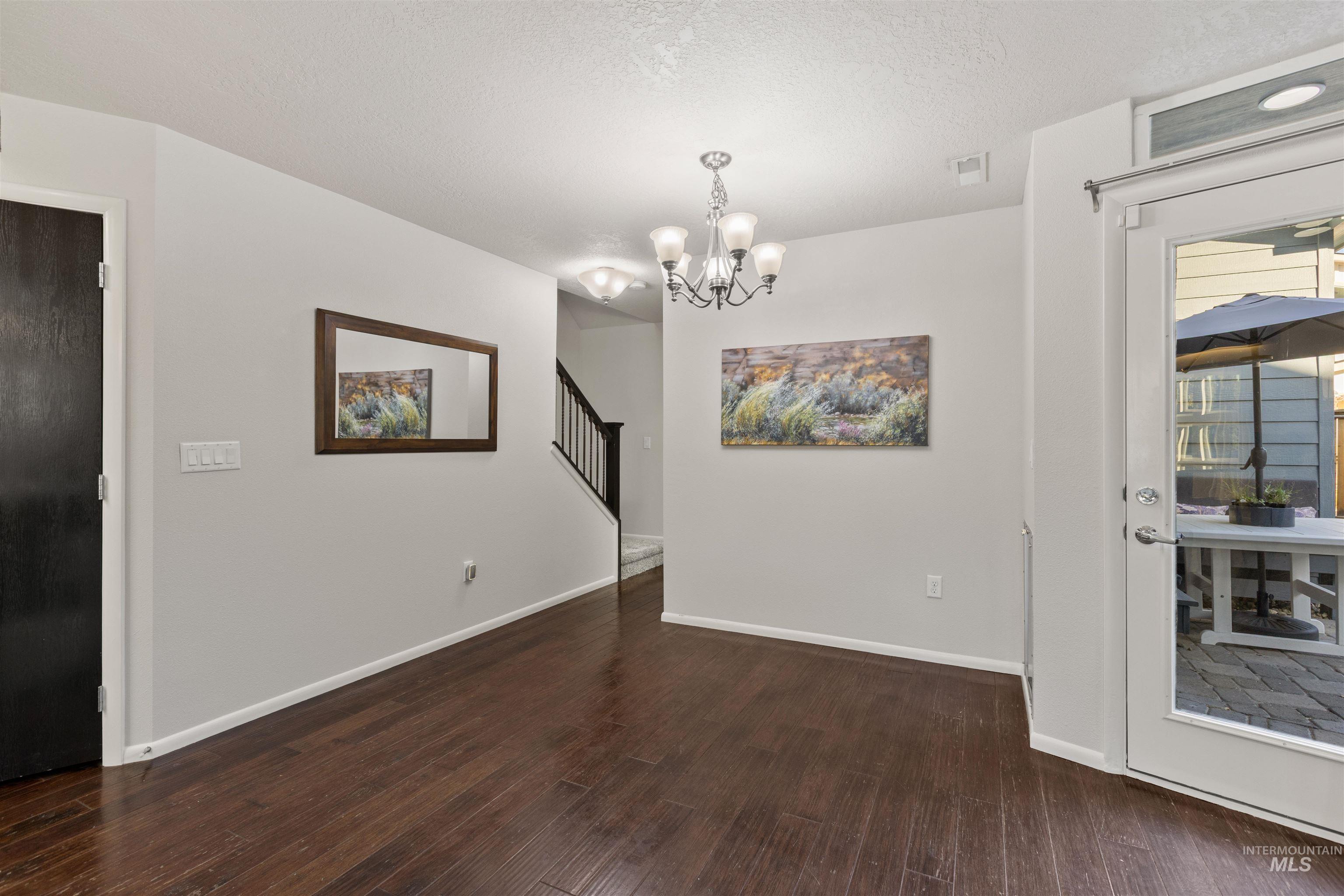 Unfurnished dining area with a chandelier, dark wood-style floors, a textured ceiling, and stairs