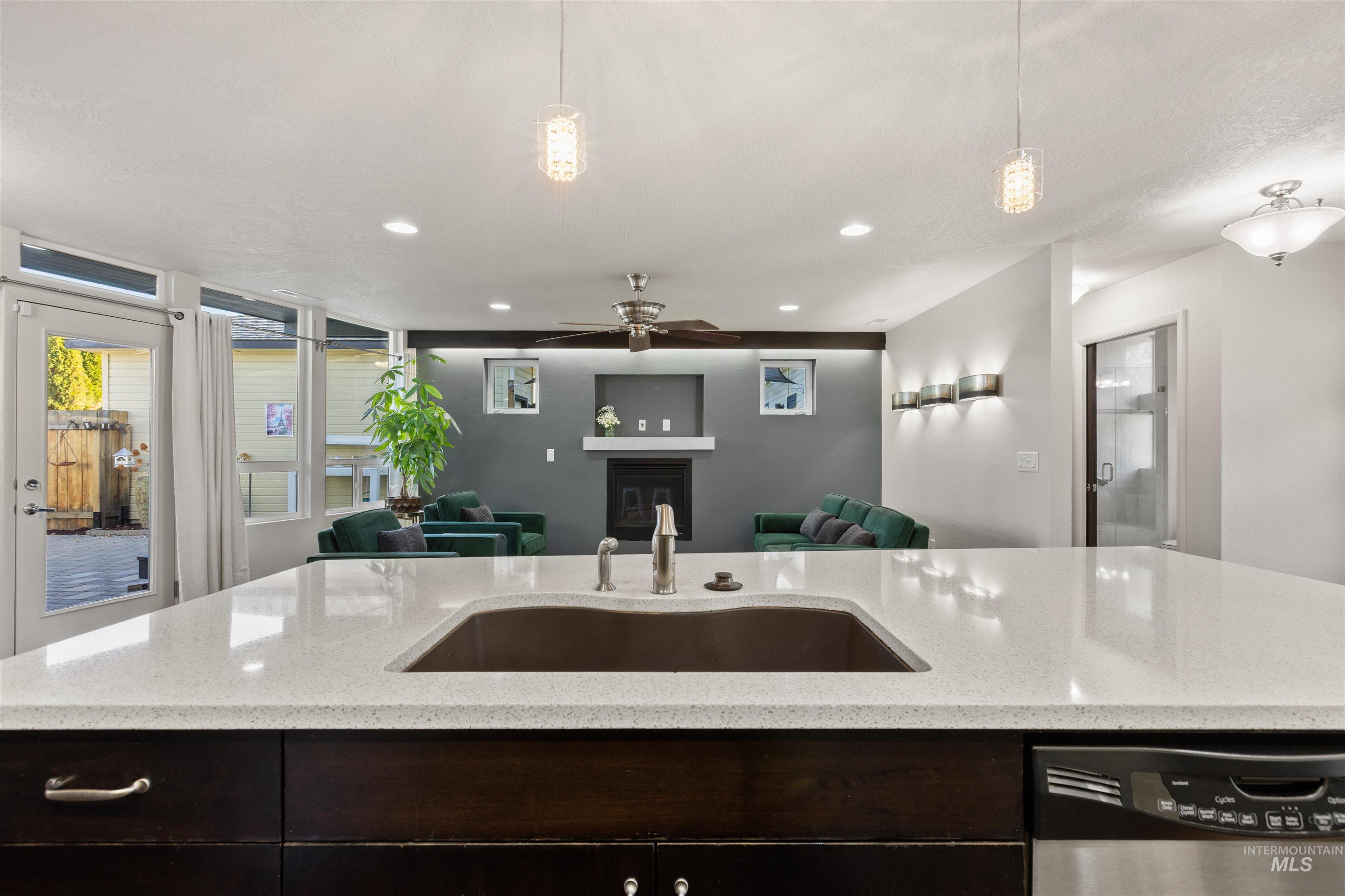 Kitchen with dark brown cabinets, dishwasher, a glass covered fireplace, light stone countertops, and recessed lighting