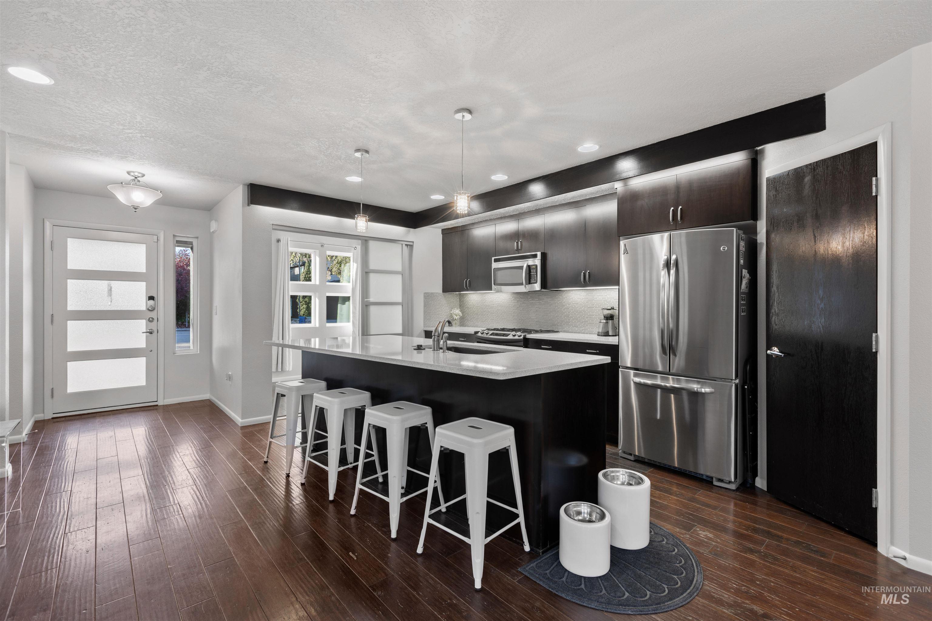 Kitchen with appliances with stainless steel finishes, a breakfast bar area, dark wood-type flooring, a kitchen island with sink, and tasteful backsplash