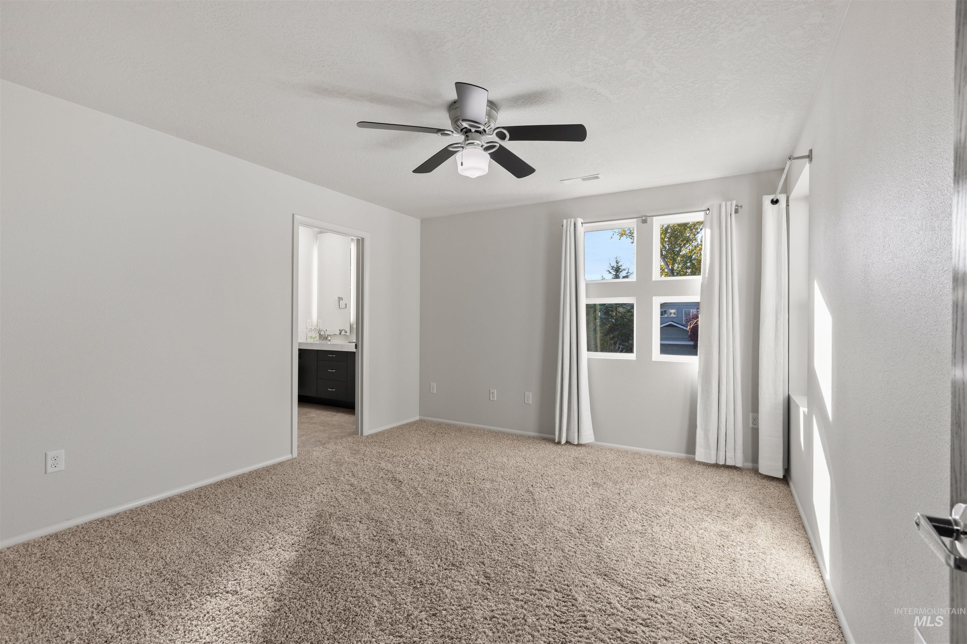 Unfurnished bedroom featuring light carpet, ensuite bath, a ceiling fan, and a textured ceiling