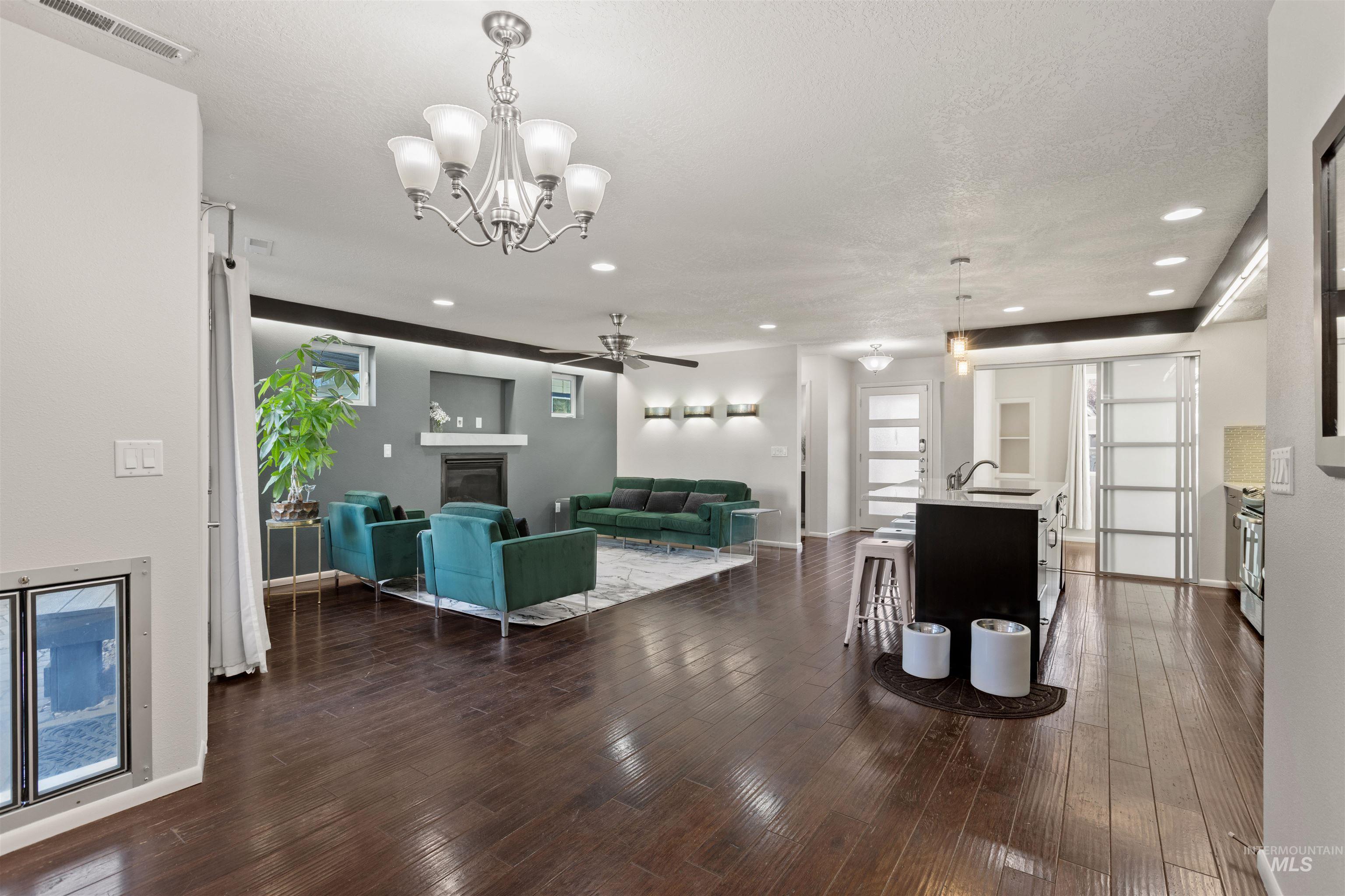 Living area with dark wood finished floors, a chandelier, healthy amount of natural light, a glass covered fireplace, and recessed lighting