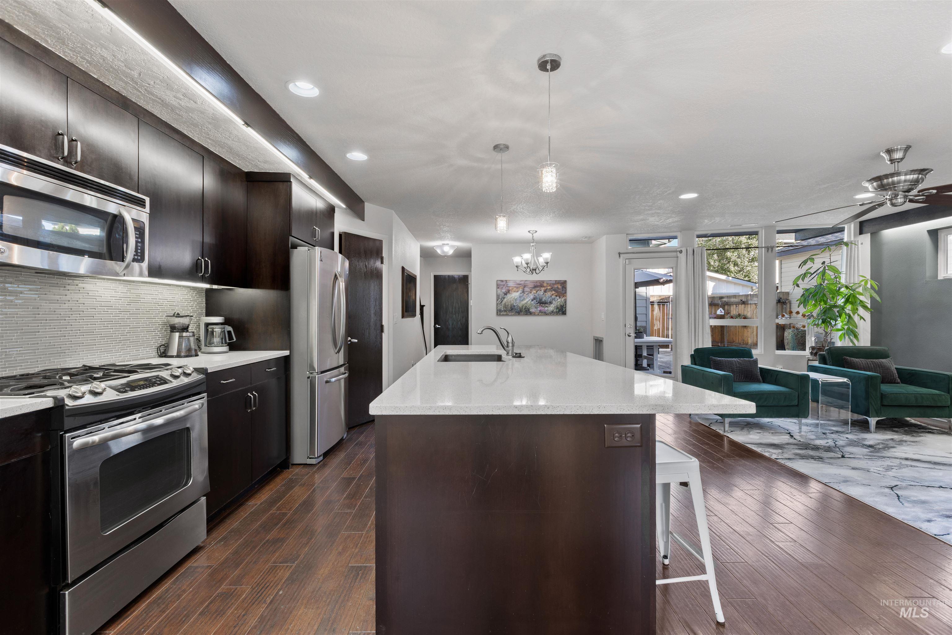 Kitchen featuring stainless steel appliances, decorative light fixtures, backsplash, open floor plan, and a kitchen breakfast bar
