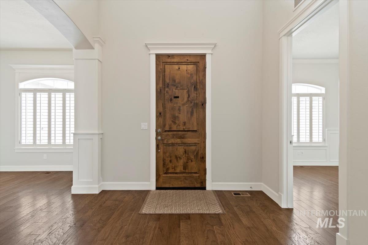 Foyer entrance featuring dark wood-type flooring, arched walkways, and crown molding
