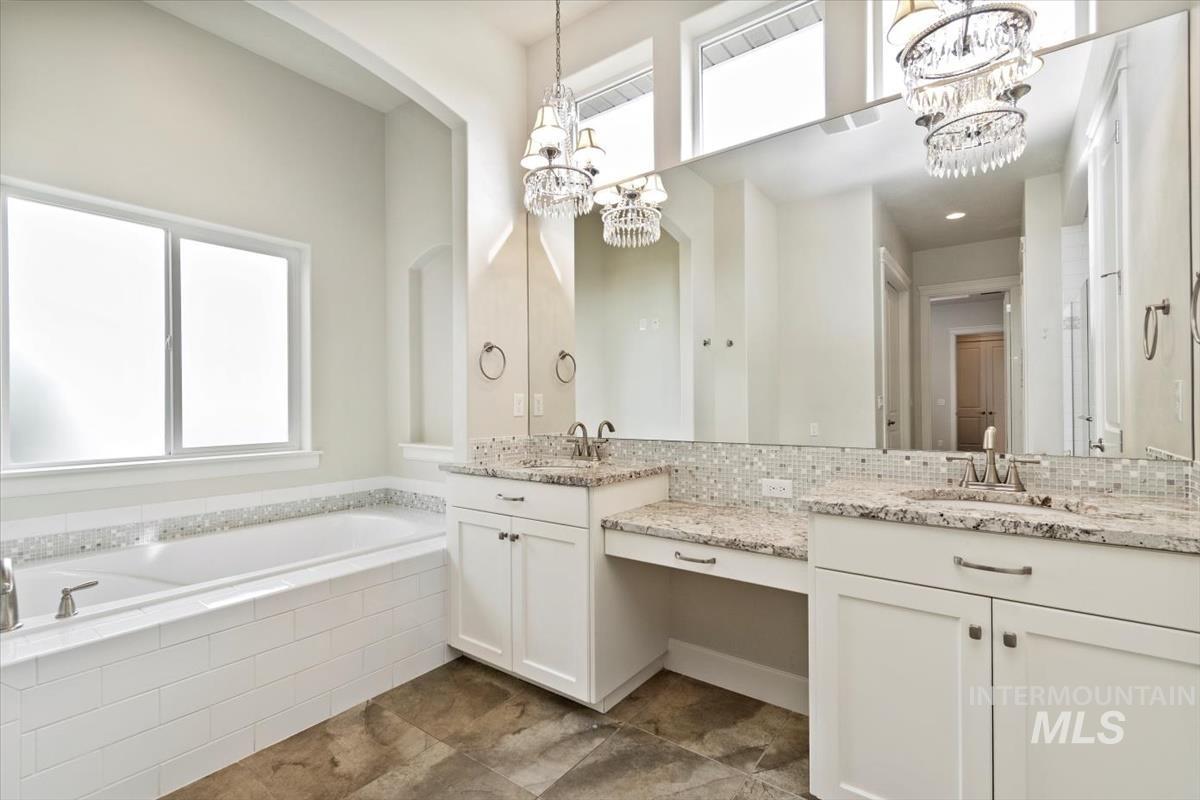 Bathroom featuring a bath, vanity, backsplash, and a chandelier