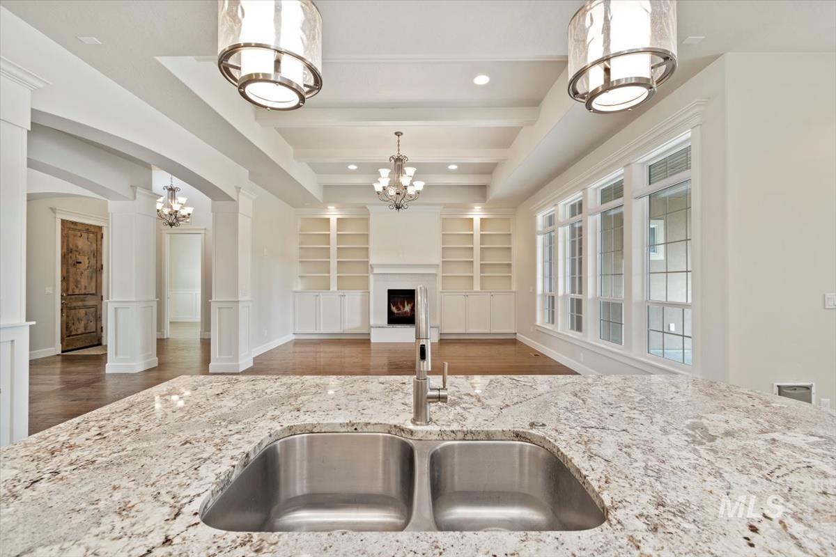 Kitchen featuring wood finished floors, a warm lit fireplace, a chandelier, beamed ceiling, and light stone countertops