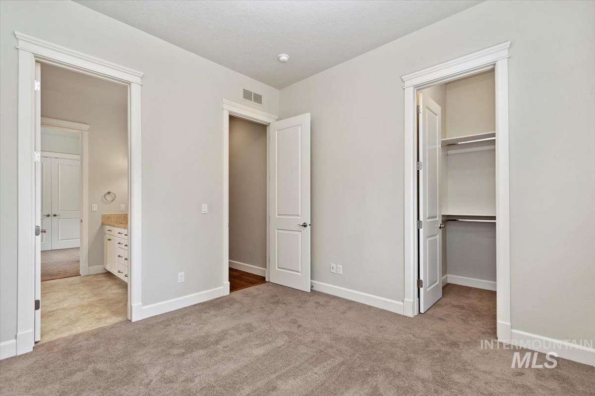 Unfurnished bedroom with a spacious closet, light carpet, and ensuite bathroom