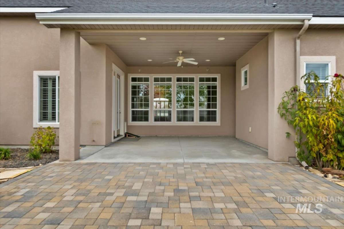 Entrance to property featuring a ceiling fan, roof with shingles, stucco siding, and a patio