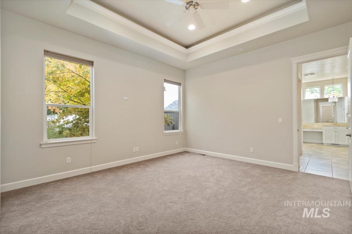 Unfurnished room featuring a raised ceiling, light colored carpet, a ceiling fan, crown molding, and recessed lighting