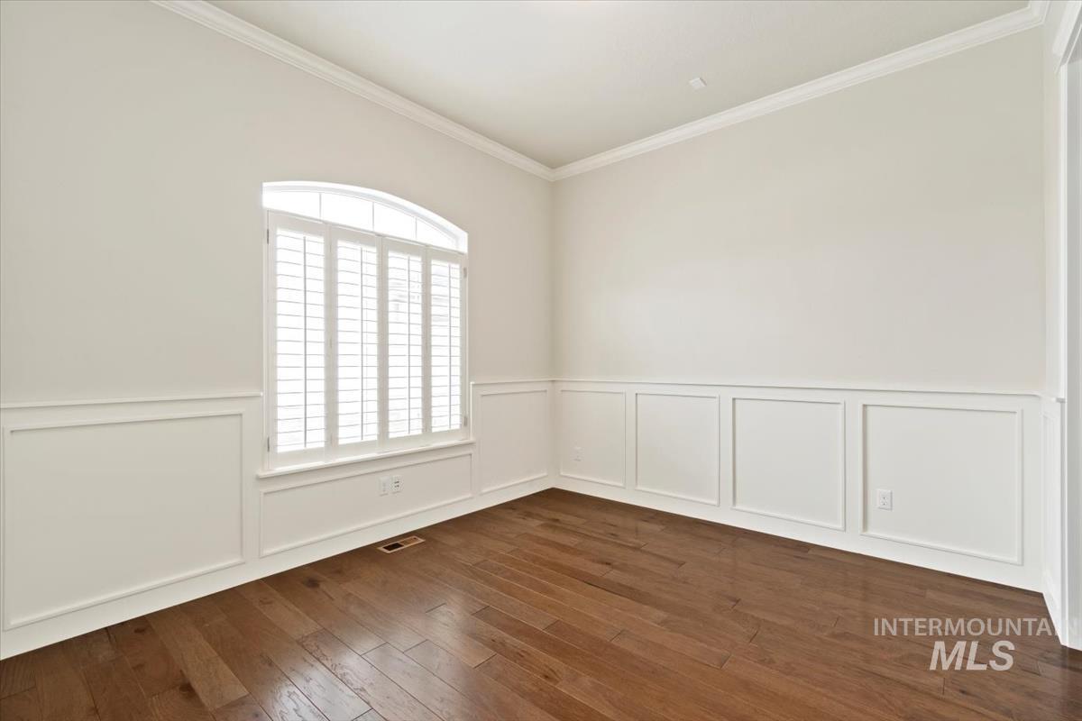 Spare room with dark wood-style flooring, crown molding, a decorative wall, and a wainscoted wall