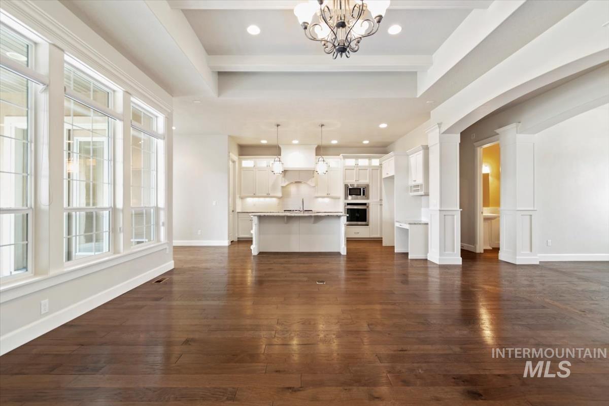 Unfurnished living room featuring a chandelier, arched walkways, dark wood-style flooring, recessed lighting, and a tray ceiling