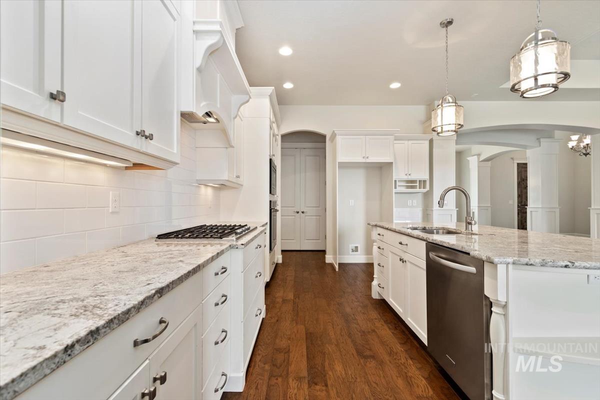 Kitchen featuring arched walkways, light stone counters, white cabinets, and recessed lighting