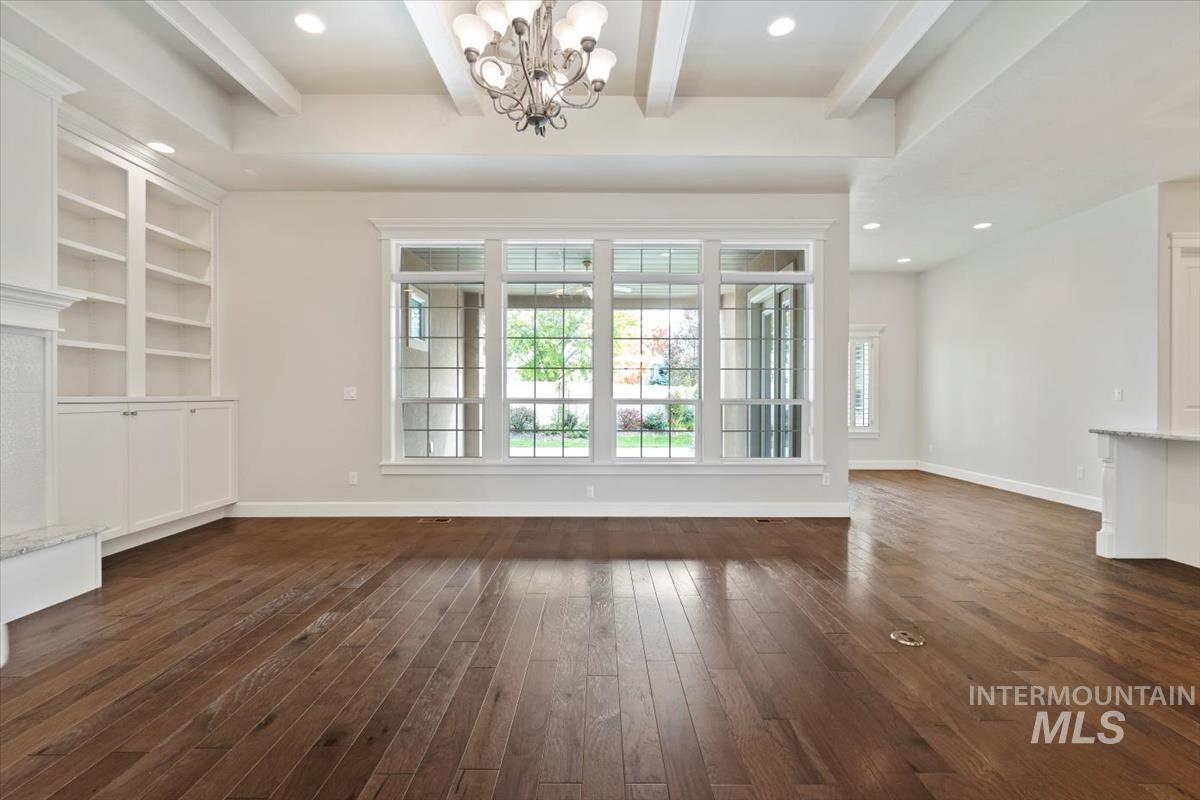 Unfurnished living room with beam ceiling, recessed lighting, plenty of natural light, a chandelier, and dark wood-type flooring