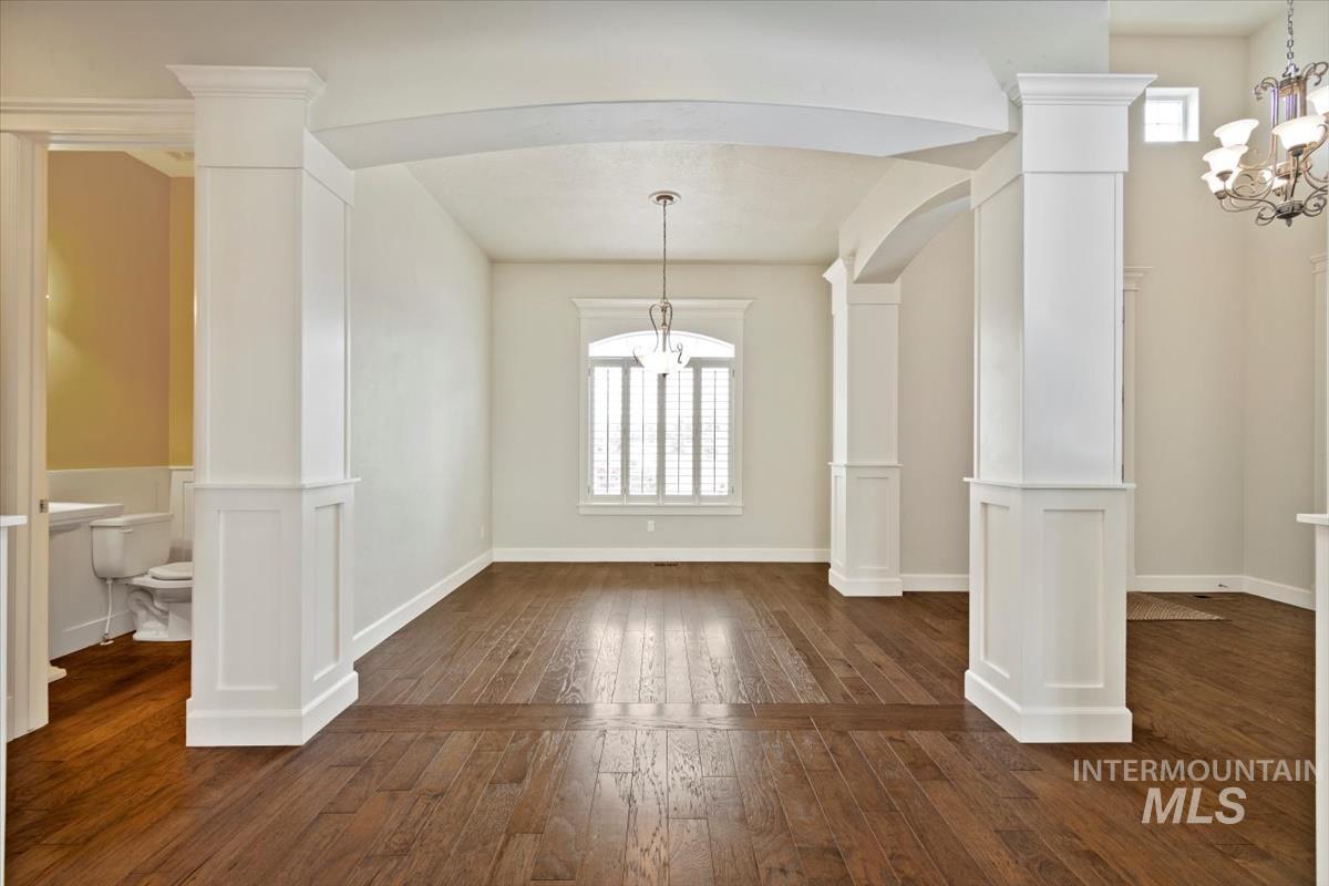 Unfurnished dining area featuring a chandelier, decorative columns, dark wood-type flooring, and a decorative wall