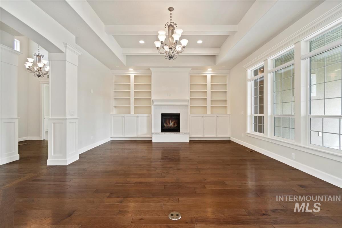 Unfurnished living room with a chandelier, dark wood-style floors, healthy amount of natural light, and beamed ceiling