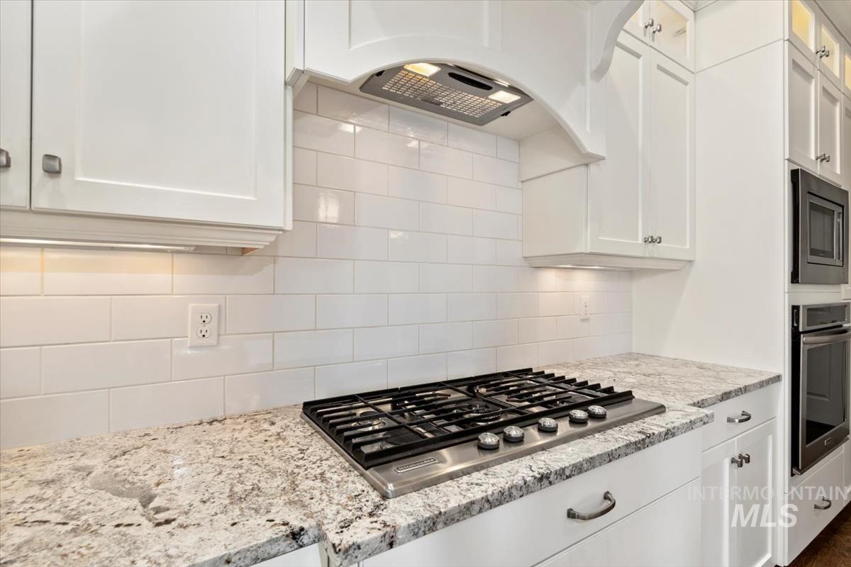 Kitchen featuring white cabinets, tasteful backsplash, stainless steel appliances, light stone countertops, and premium range hood