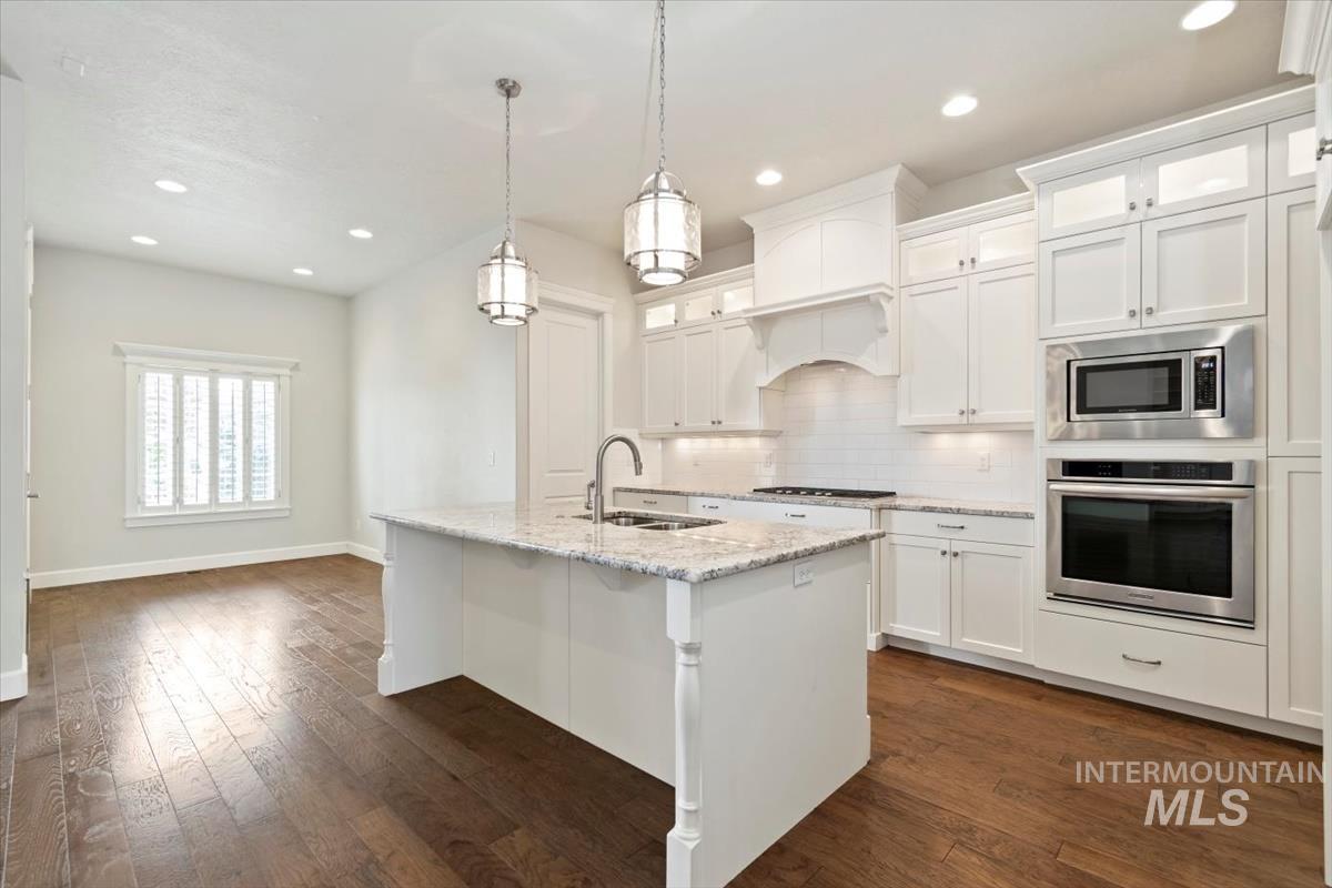 Kitchen featuring backsplash, stainless steel appliances, white cabinetry, light stone counters, and recessed lighting