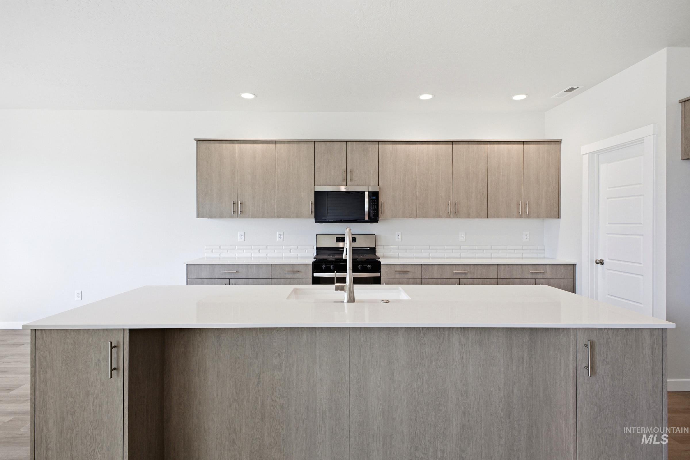 Kitchen featuring a large island with an undermount sink, light wood-finish cabinetry, white subway tile backsplash, stainless steel microwave, and gas range