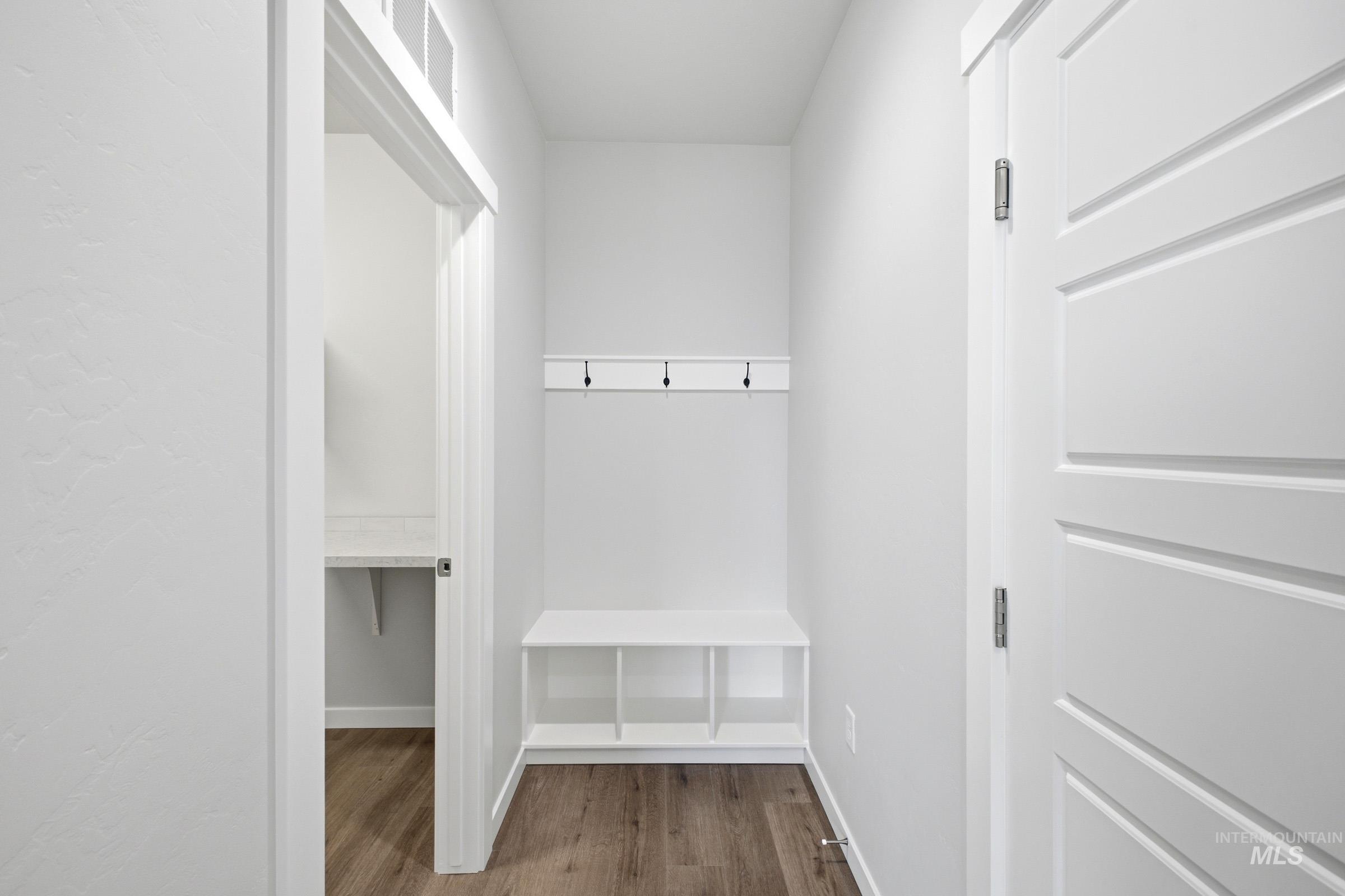Entryway featuring built-in white bench seating with cubby storage, wall-mounted coat hooks, and wood-finish flooring