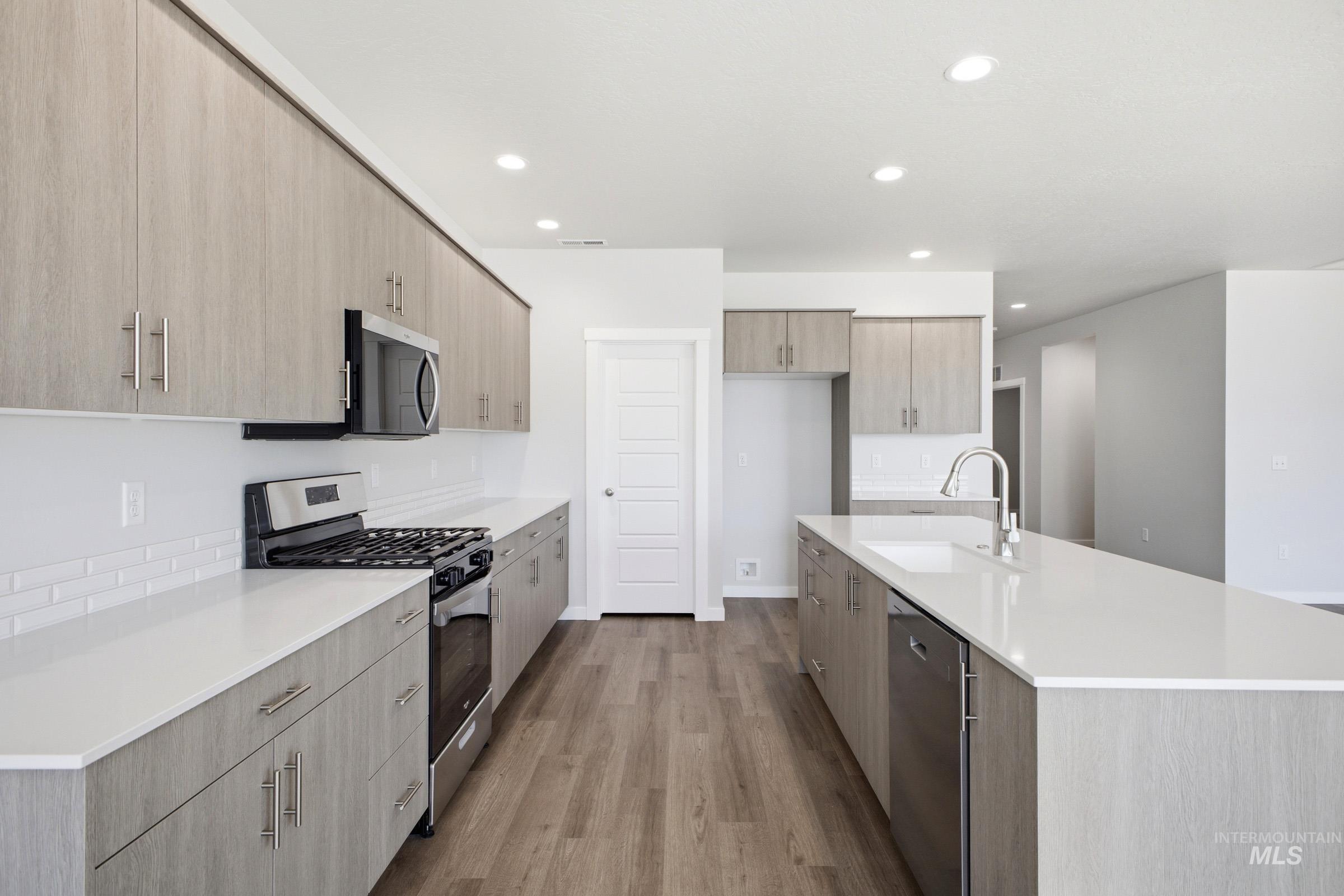 Modern kitchen featuring wood-finish flooring, light wood-grain cabinetry, white countertops, a subway tile backsplash, and stainless steel appliances
