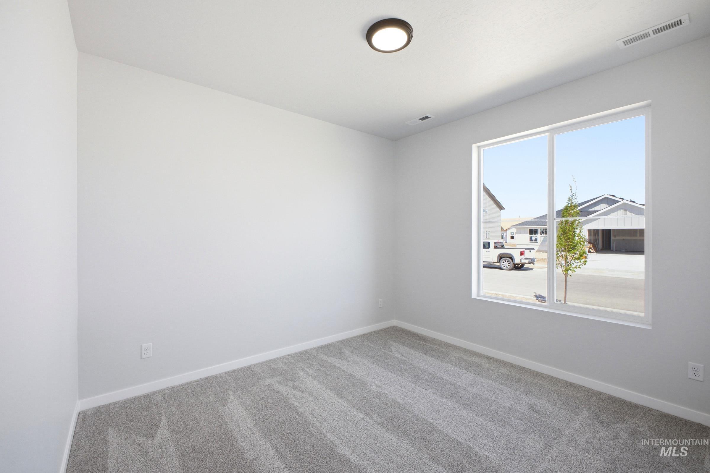 Light-filled room featuring a large window, neutral wall paint, gray patterned carpeting, and a flush-mount ceiling light fixture