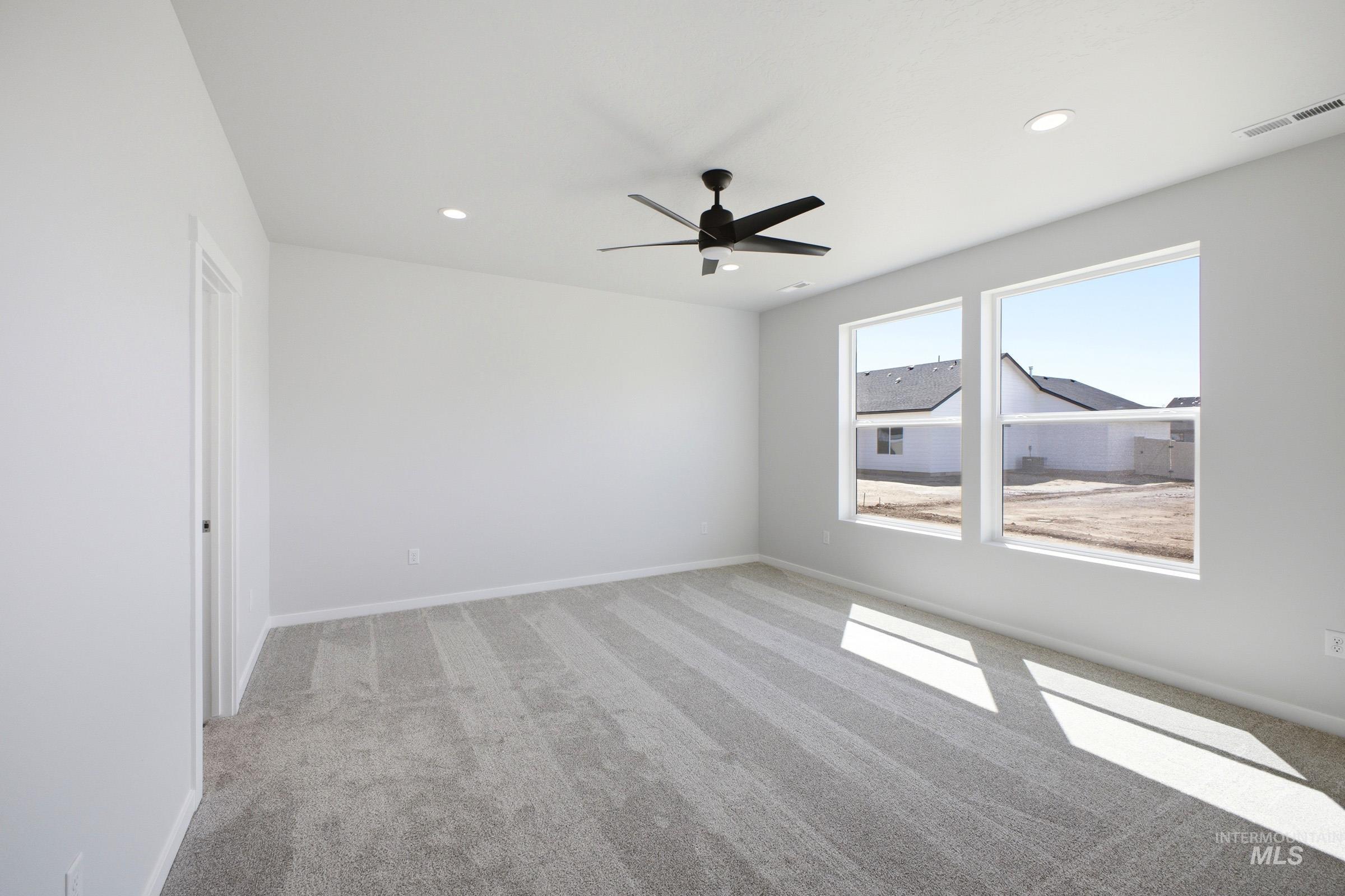 Spacious room featuring two large windows, gray patterned carpeting, a contemporary black ceiling fan with integrated lighting, and recessed ceiling lights