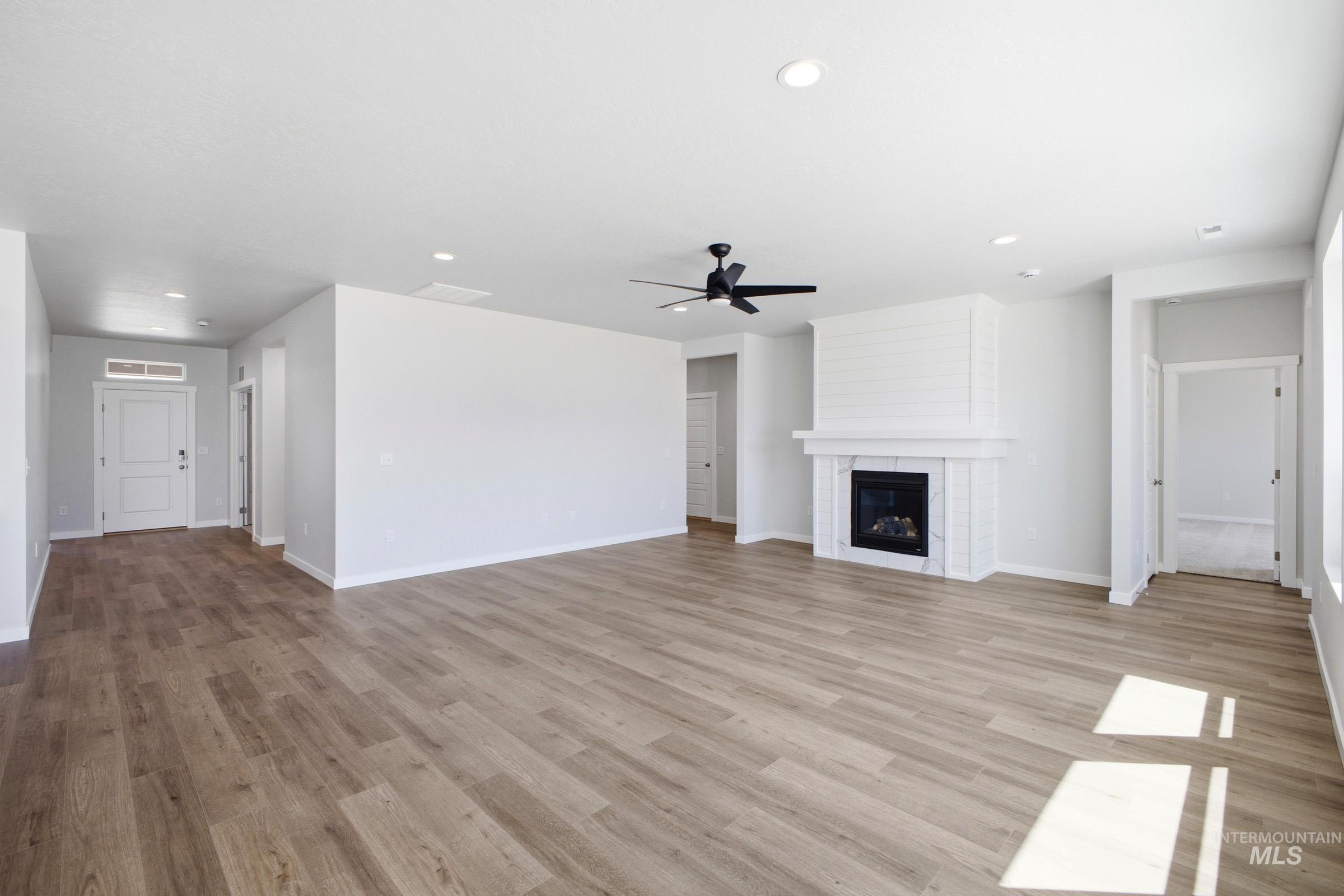 Spacious living area featuring wood-finish flooring, a white mantel fireplace with a dark insert, a ceiling fan, and recessed lighting