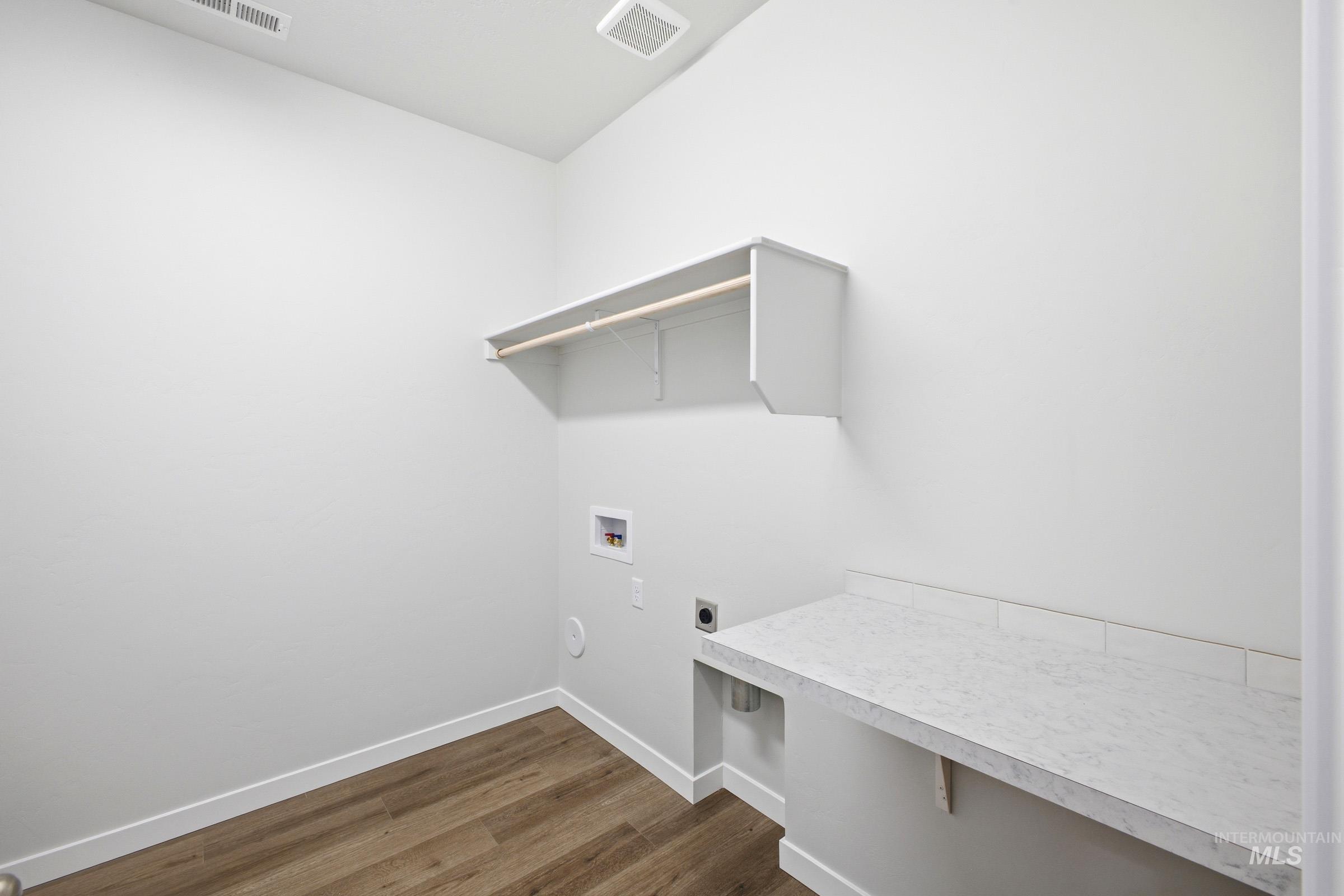 Utility room featuring wood-finish flooring, white baseboards, a built-in shelf with hanging rod, and a spacious countertop with a tiled backsplash