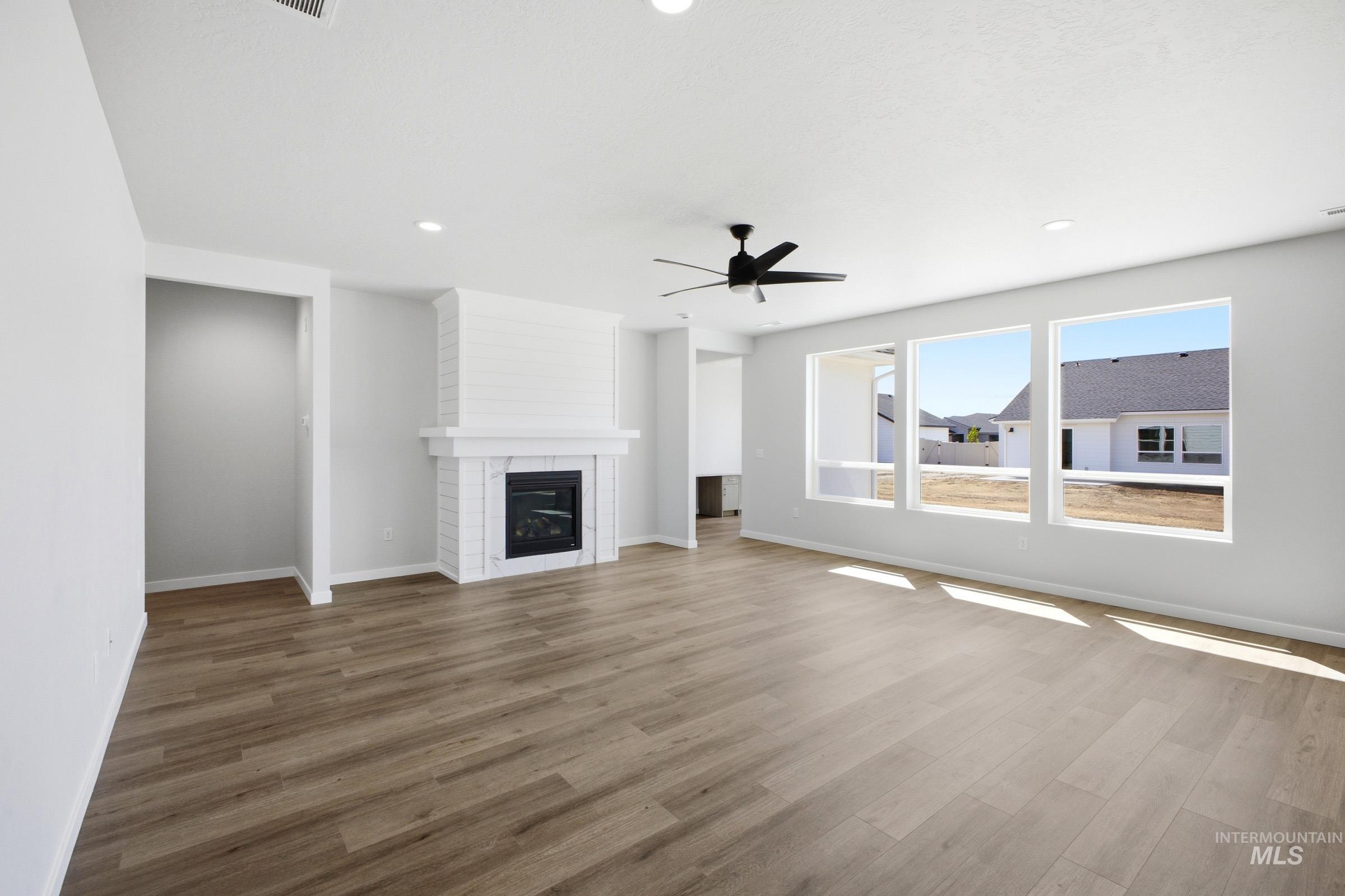 Open-concept living space featuring wood-finish flooring, a white brick fireplace with mantel, and recessed lighting