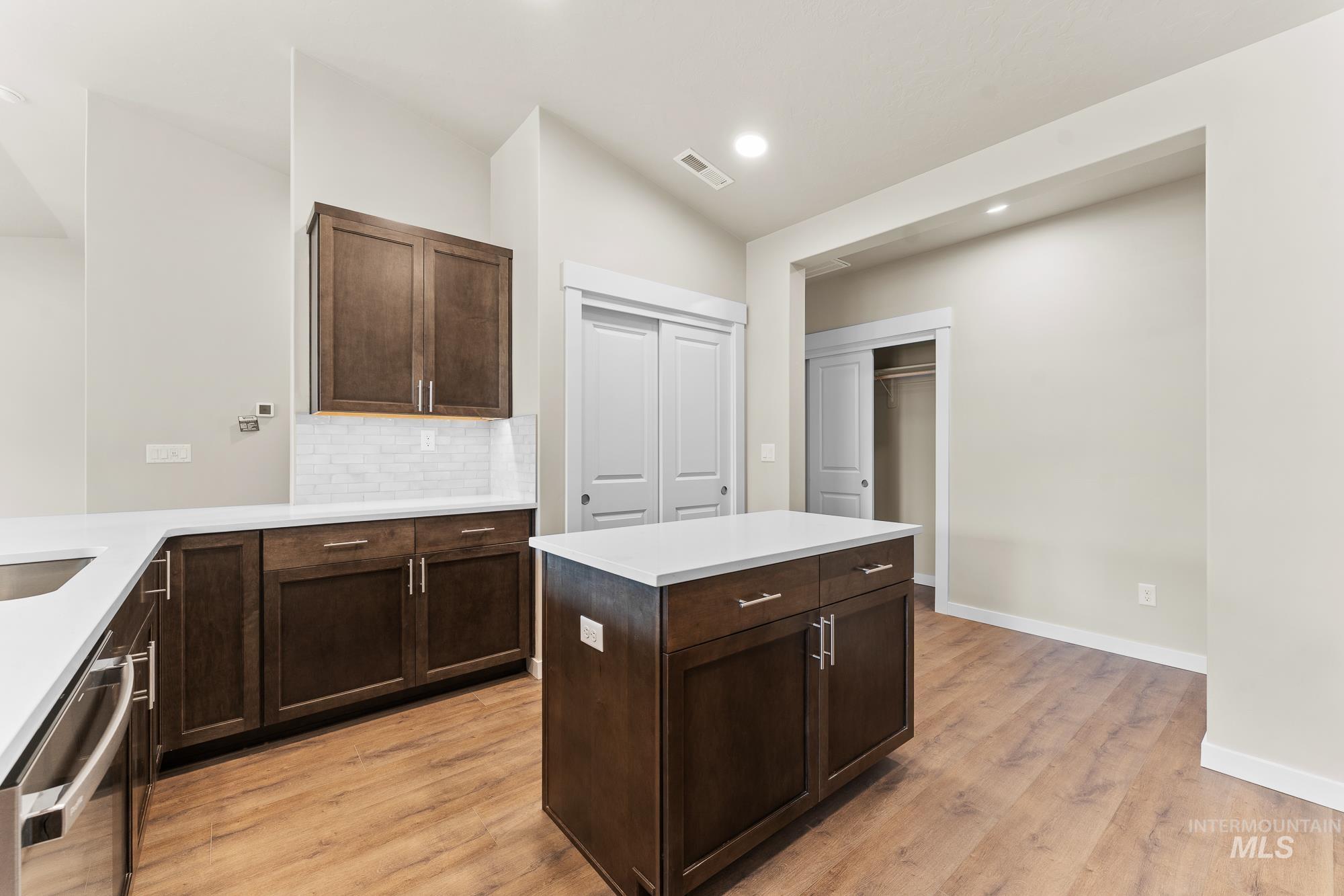 Modern kitchen featuring a central island with white countertop, dark wood-finish cabinetry, and stainless steel hardware