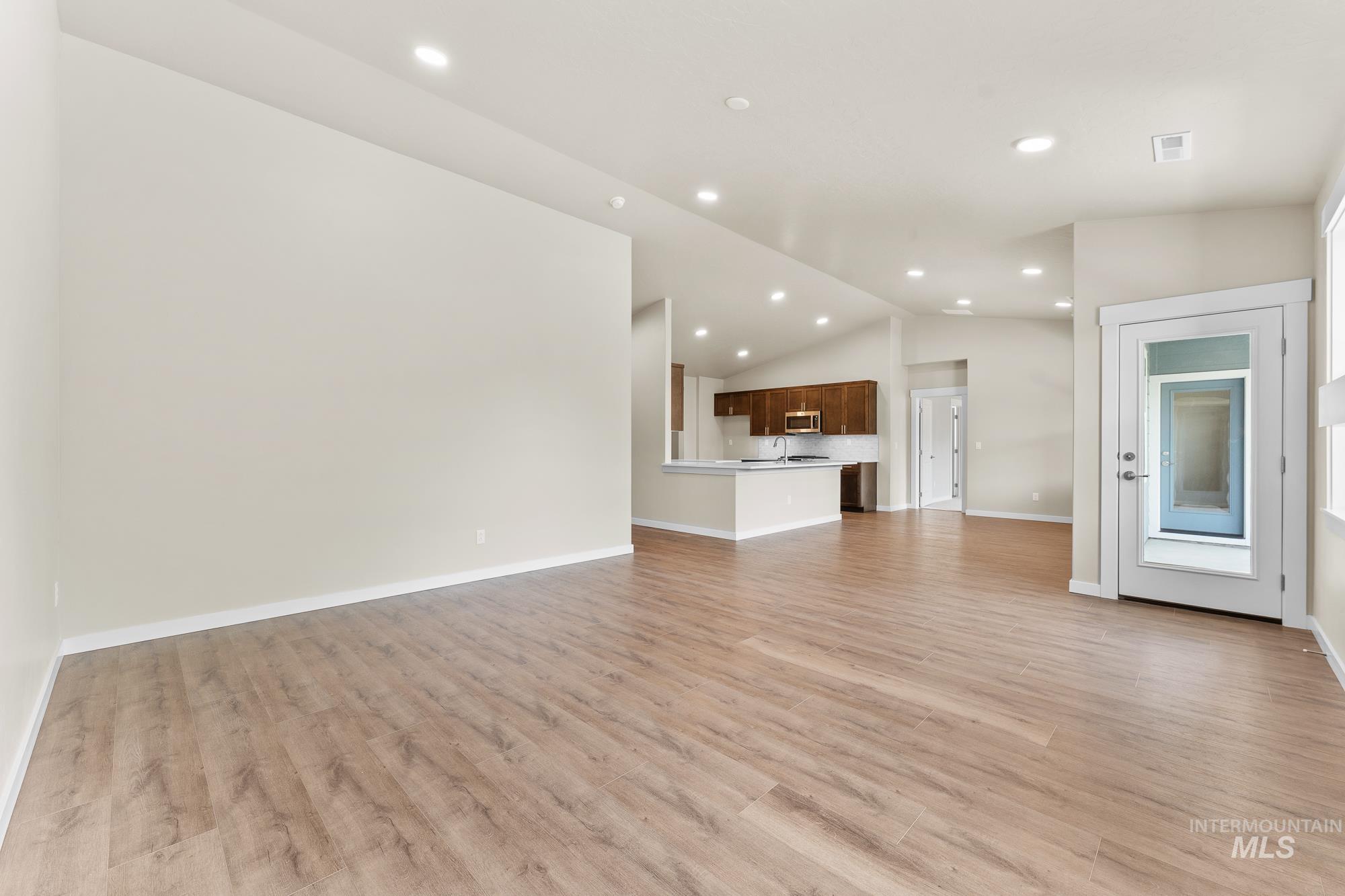 Spacious open-concept living area featuring wood-finish flooring, recessed lighting, and a vaulted ceiling