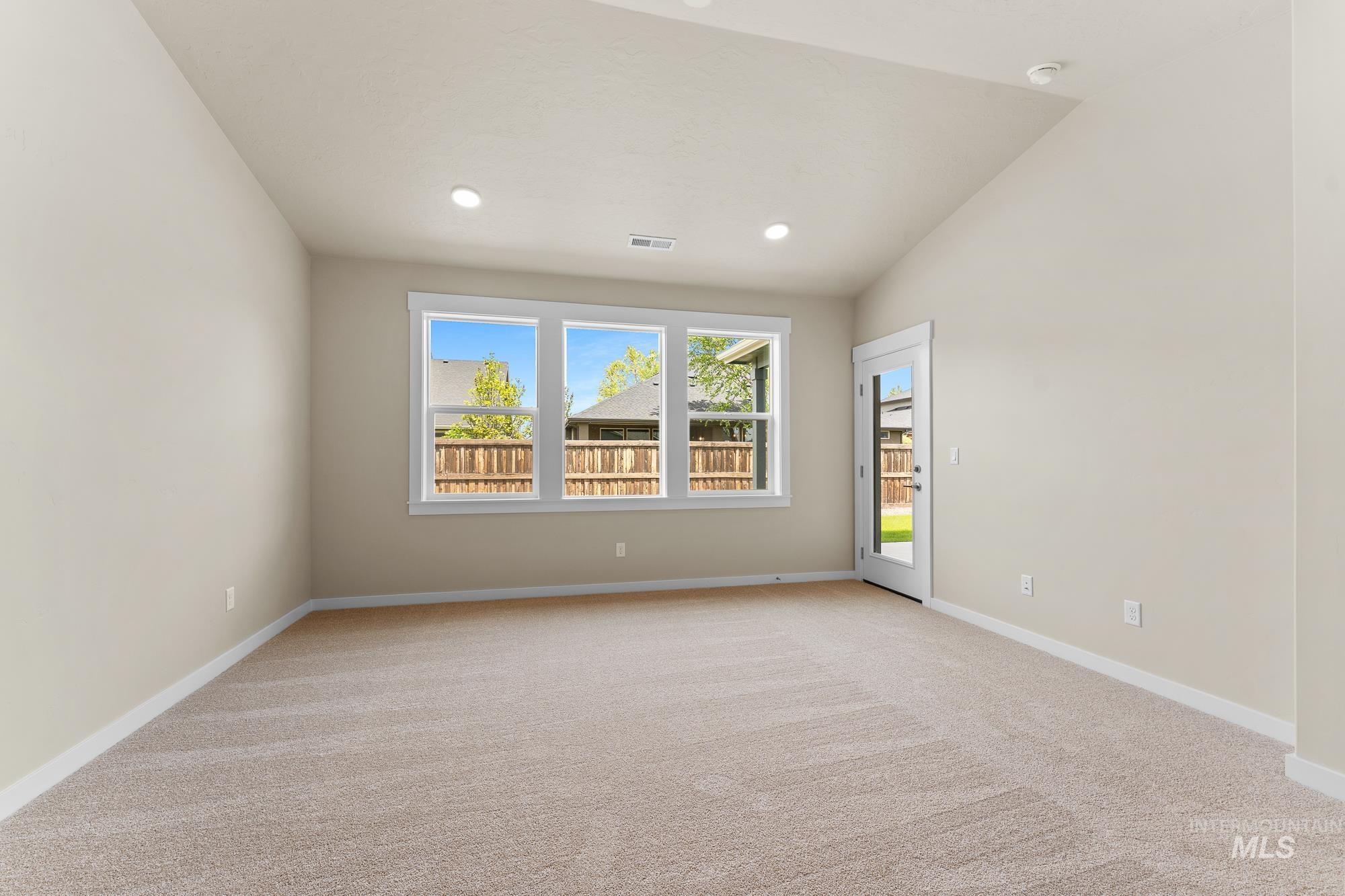 Carpeted room featuring a vaulted ceiling with recessed lighting, three large windows, a white framed glass-paneled door, and neutral wall tones