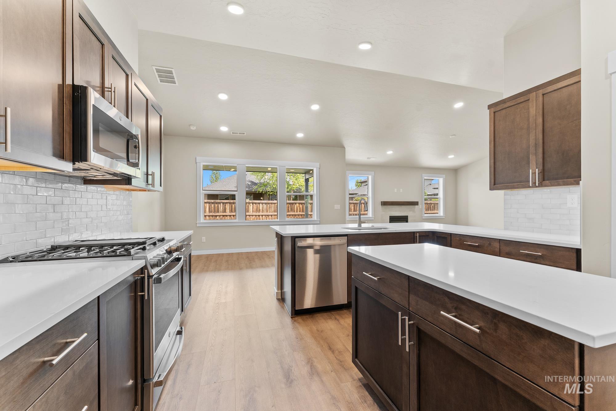 Contemporary kitchen featuring dark wood cabinetry, white countertops, stainless steel appliances, and a subway tile backsplash