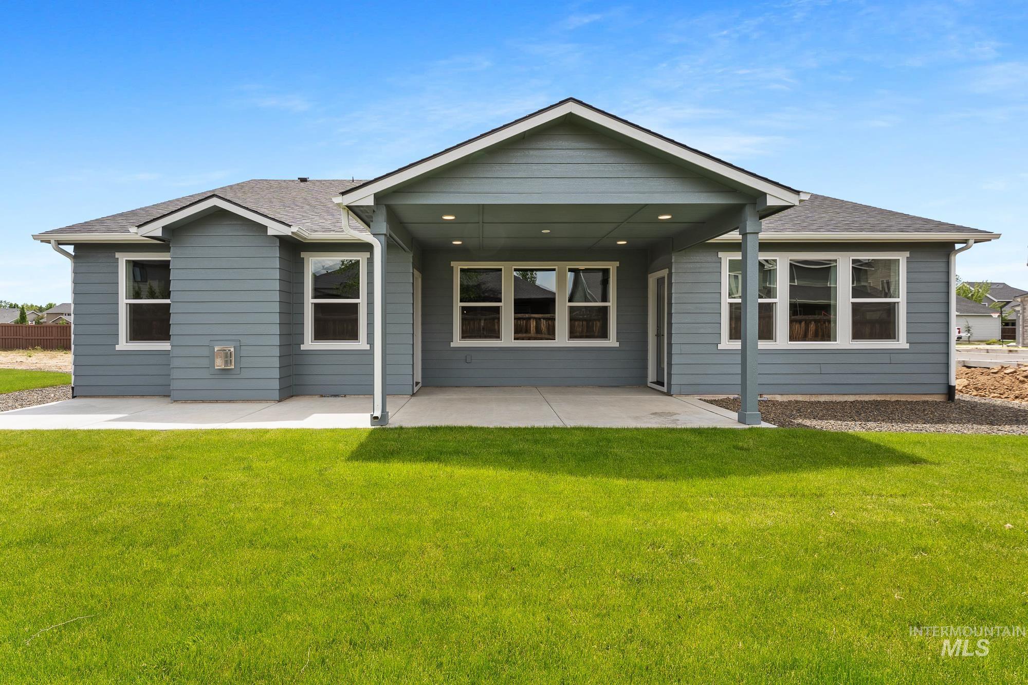 Rear exterior featuring a covered patio, multiple windows, and a manicured lawn
