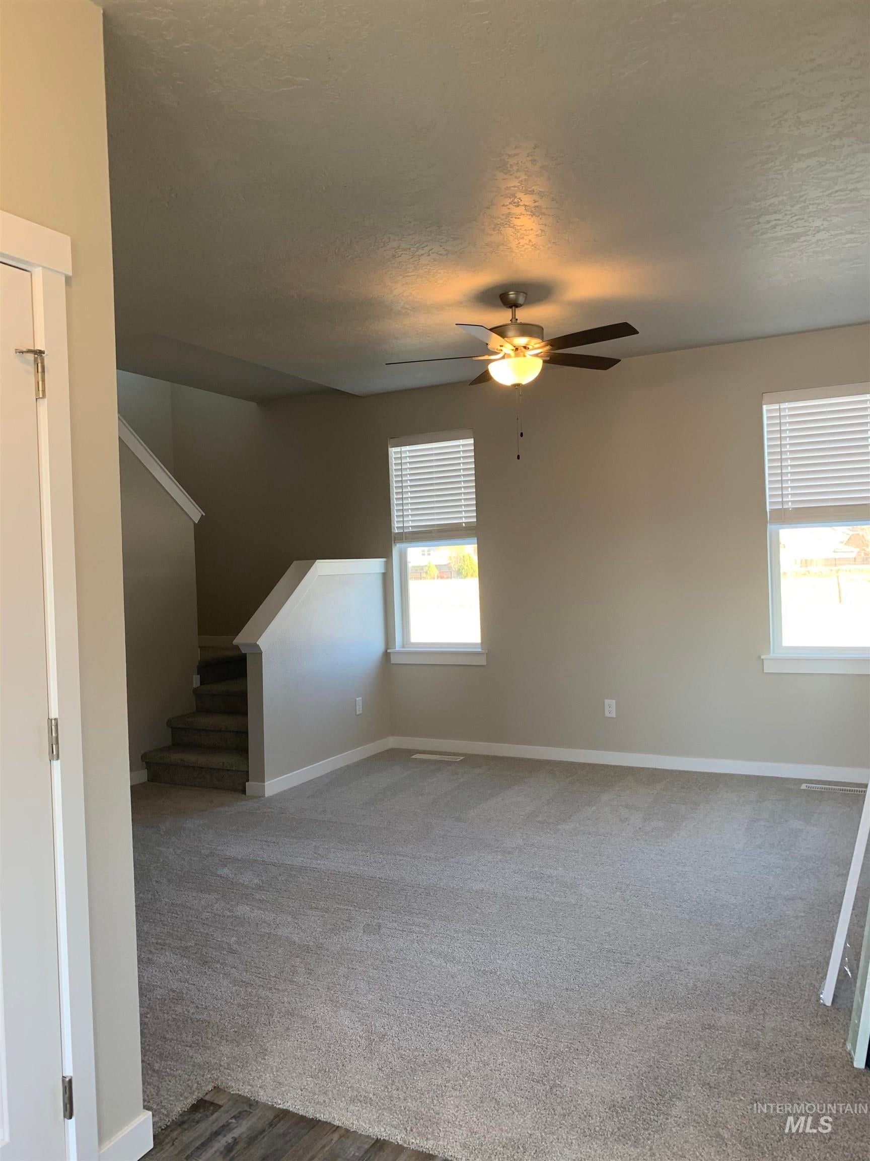Unfurnished living room featuring carpet floors, a textured ceiling, and a ceiling fan