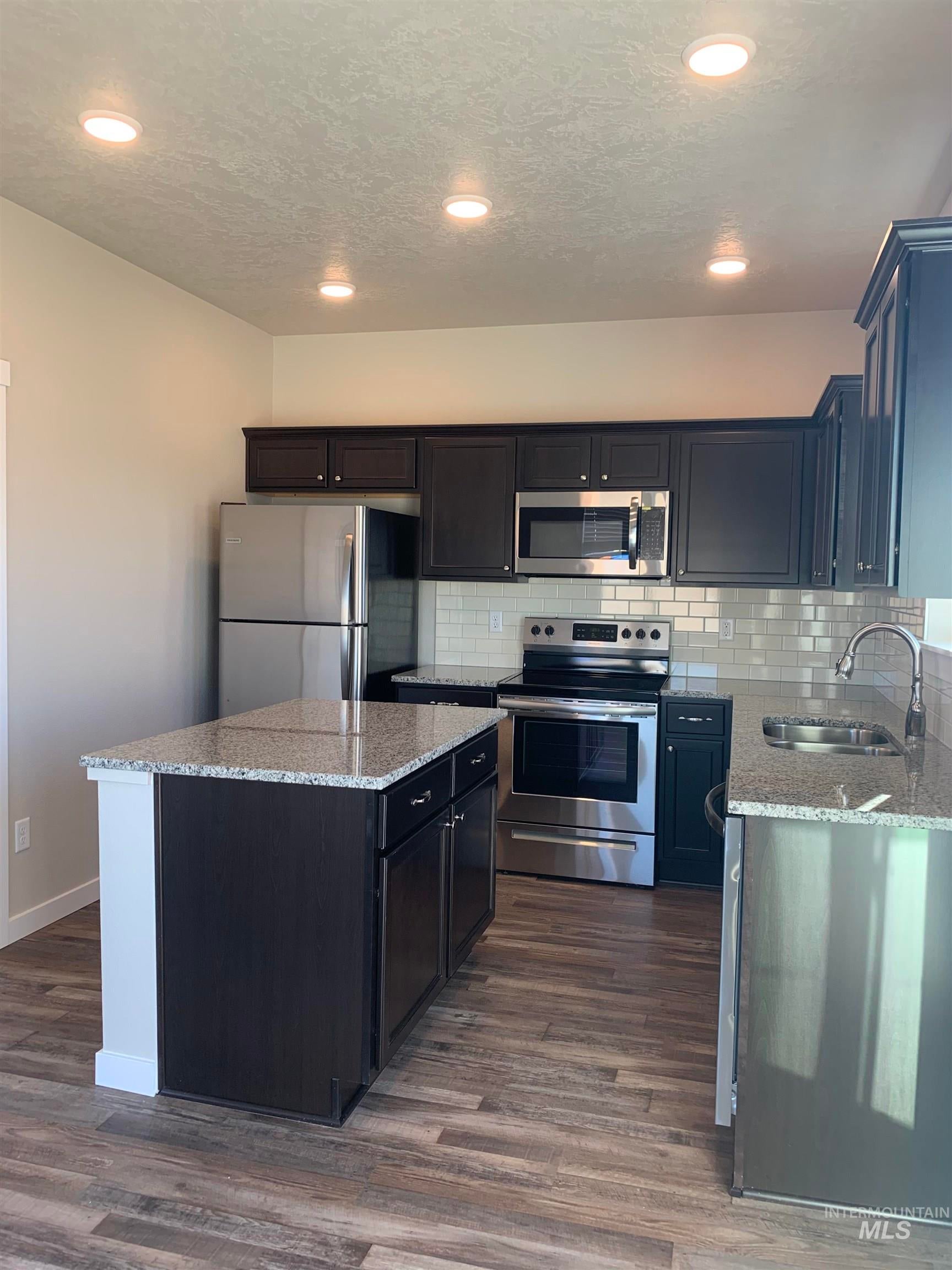 Kitchen featuring stainless steel appliances, light stone counters, a center island, tasteful backsplash, and dark wood finished floors