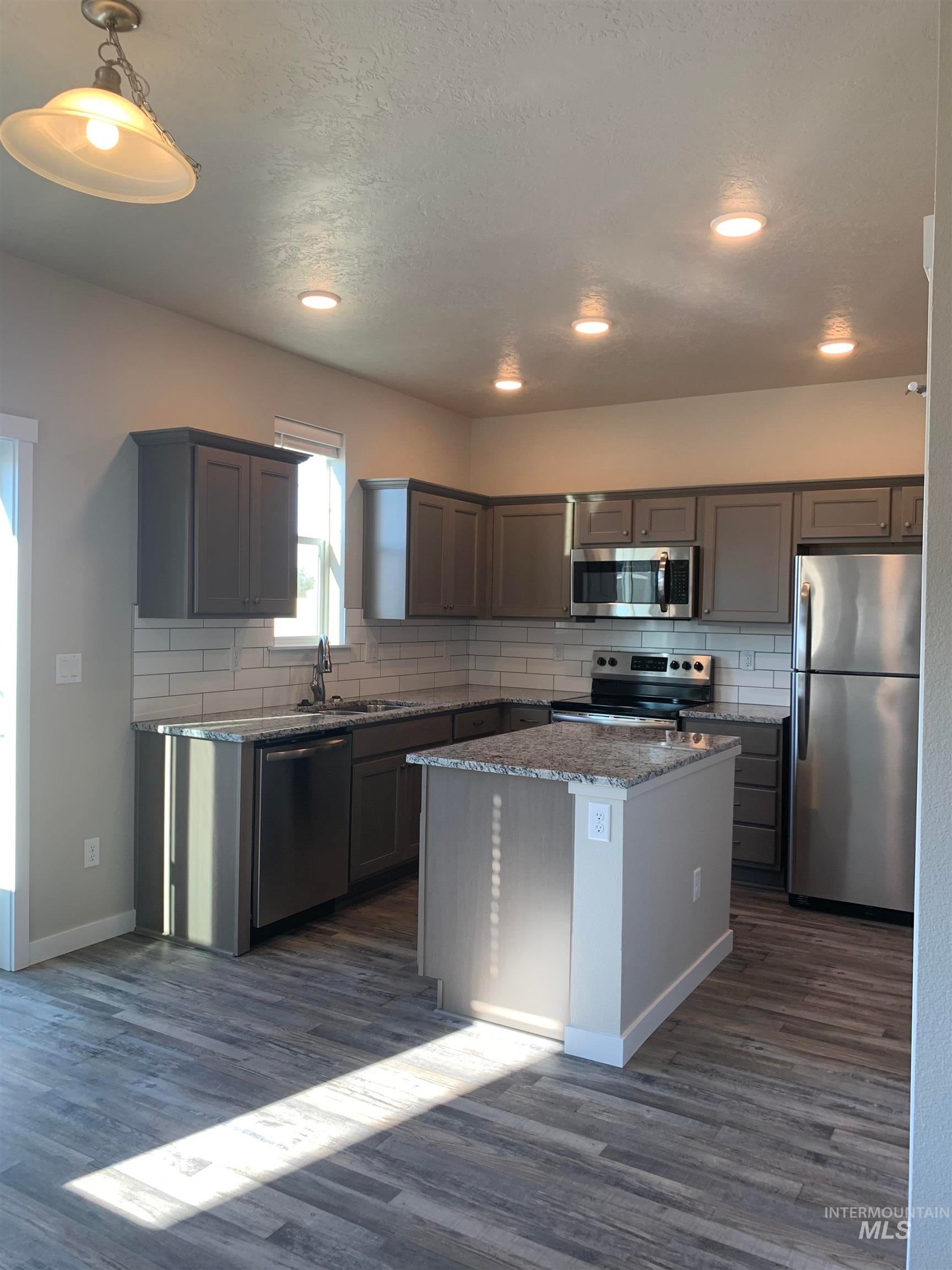 Kitchen featuring decorative backsplash, stainless steel appliances, light stone counters, a center island, and dark wood-type flooring