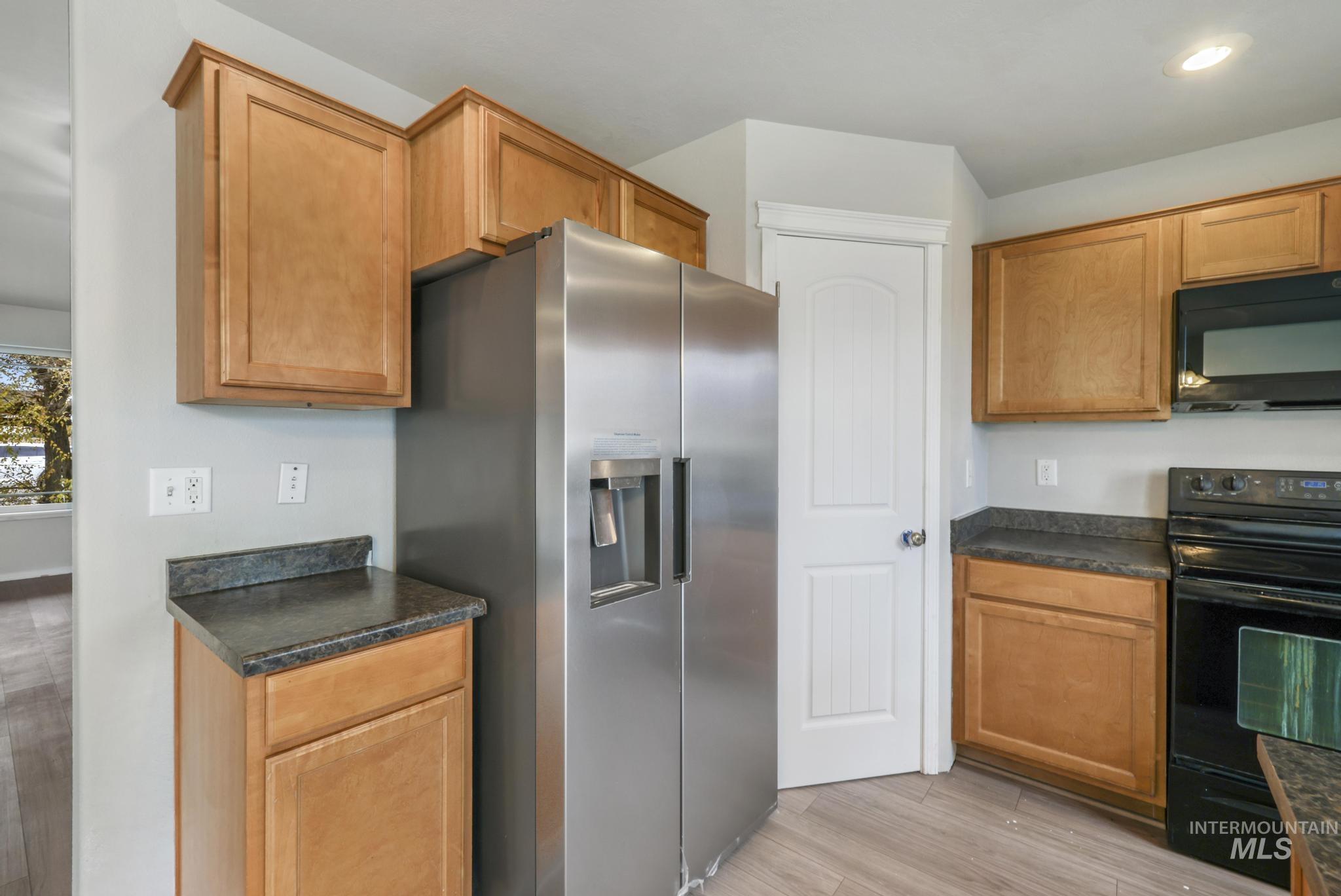 Kitchen with black appliances, dark countertops, light wood-type flooring, brown cabinetry, and recessed lighting