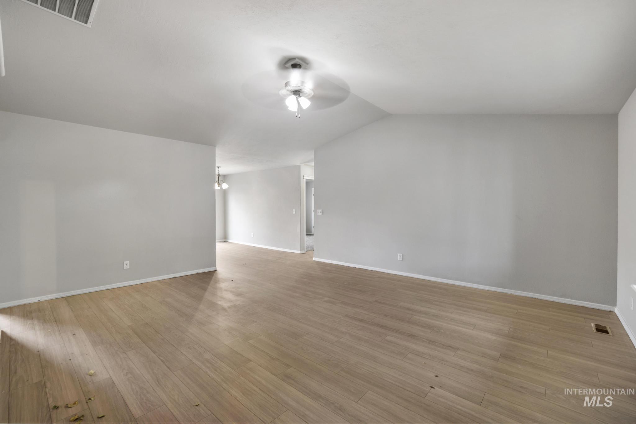 Empty room featuring light wood-style floors, a ceiling fan, a chandelier, and vaulted ceiling