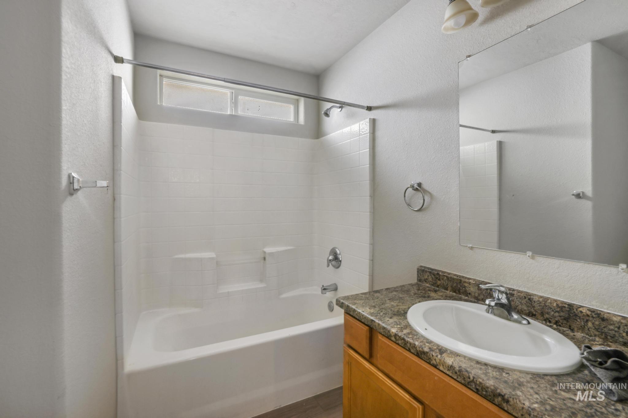Bathroom with a textured wall, vanity, shower / bathtub combination, and dark wood-style floors