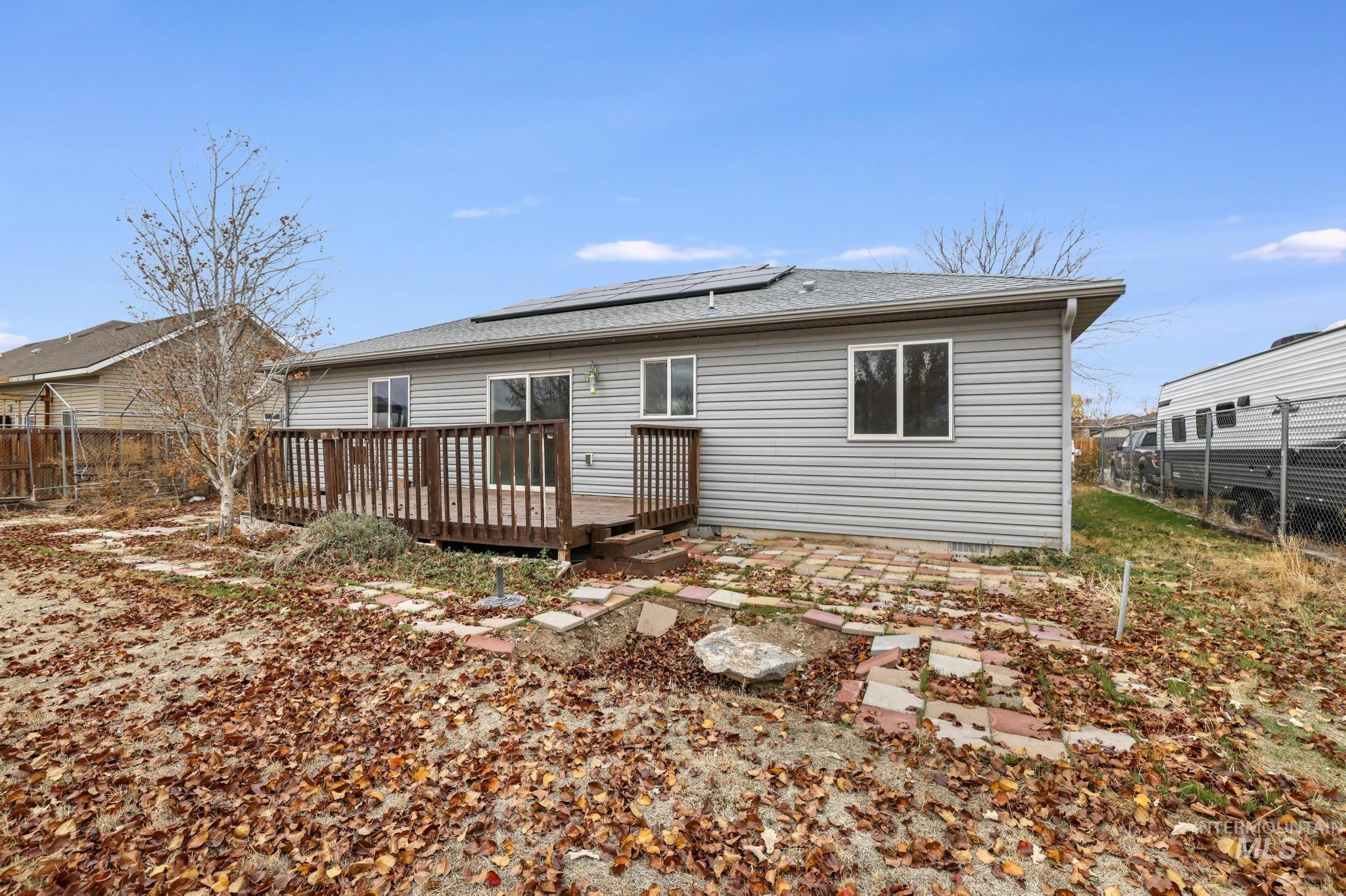 Back of property with a wooden deck, a shingled roof, and solar panels
