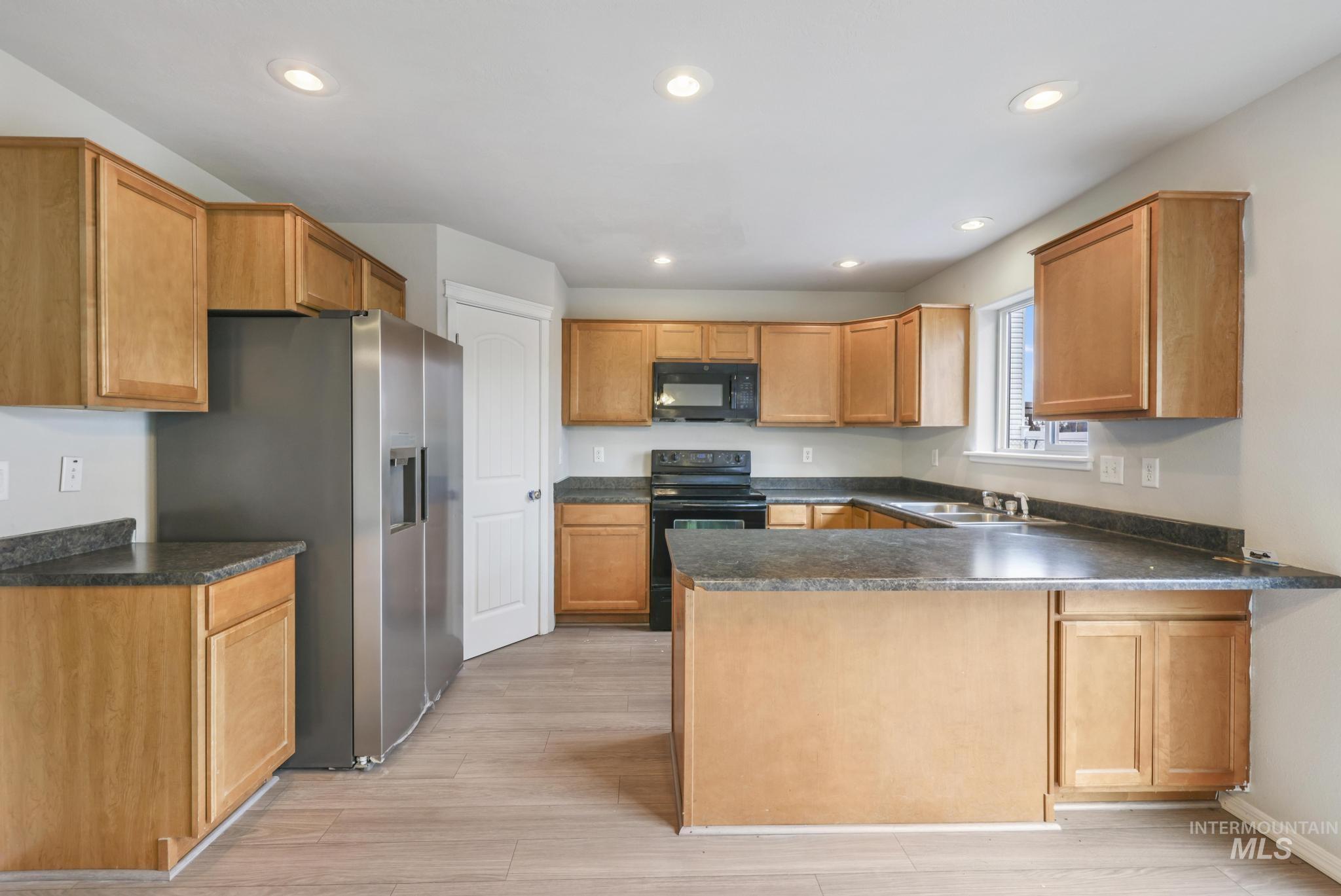 Kitchen with dark countertops, black appliances, a peninsula, recessed lighting, and brown cabinets