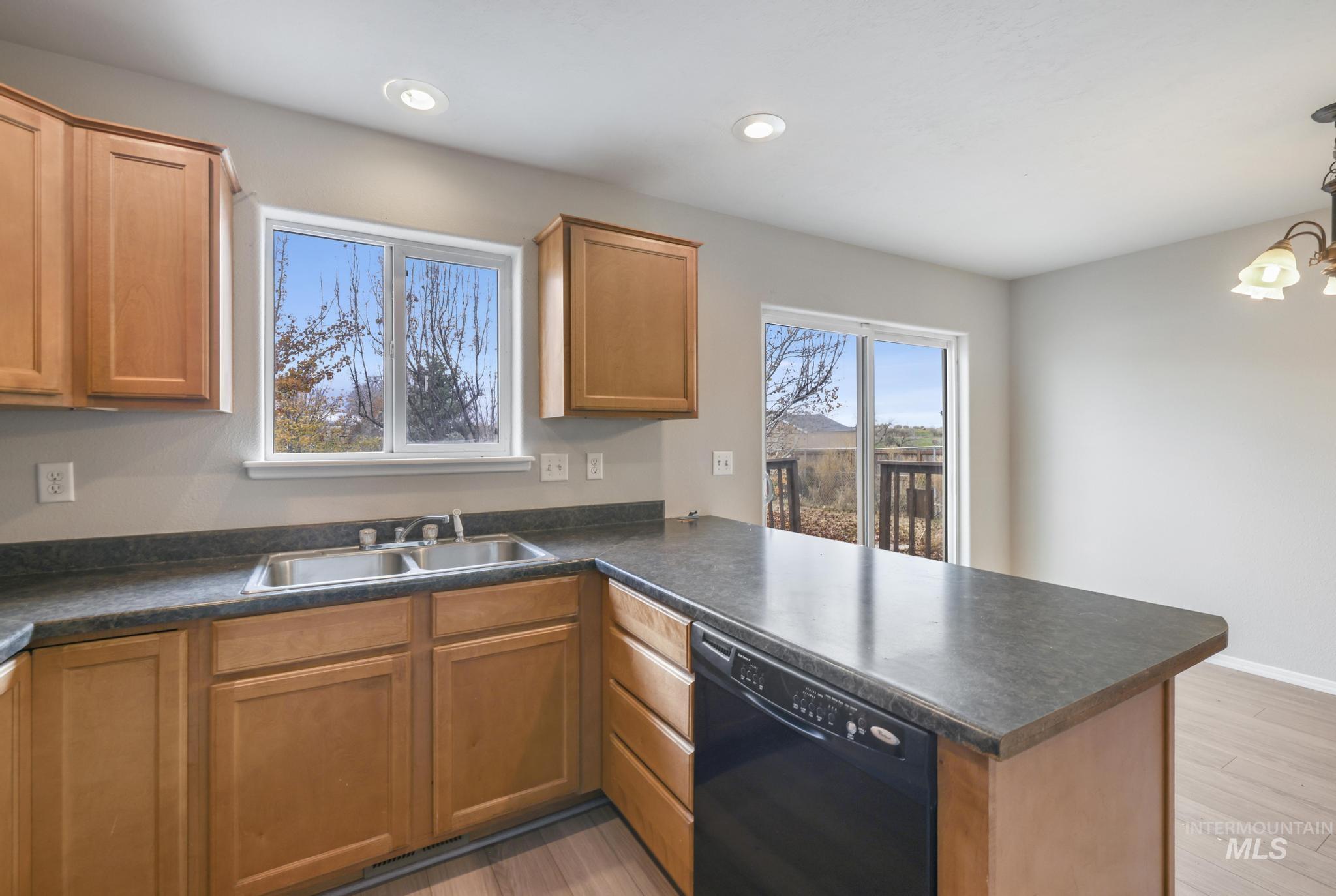 Kitchen featuring dishwasher, a peninsula, dark countertops, light wood finished floors, and a chandelier