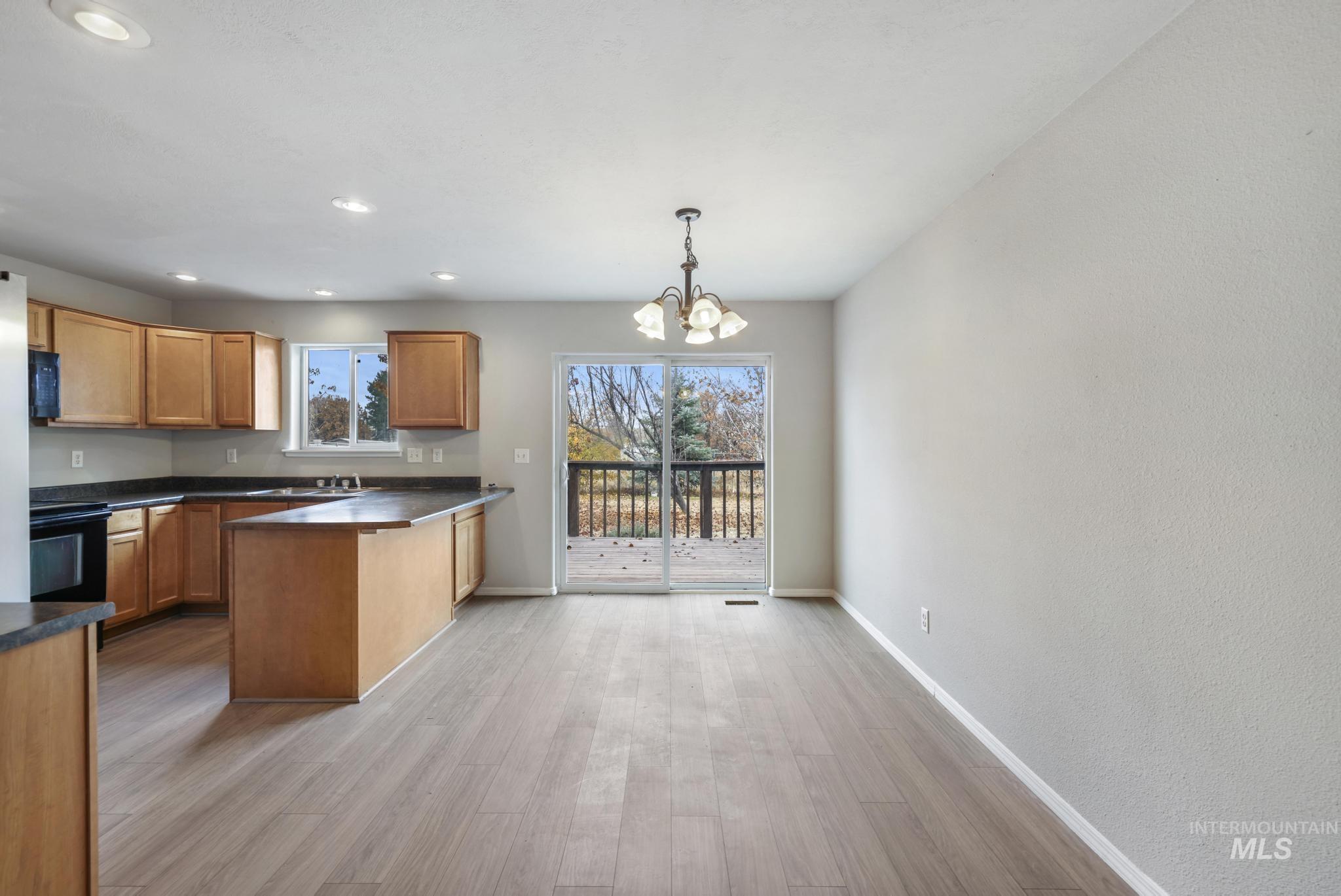 Kitchen featuring brown cabinetry, dark countertops, a peninsula, pendant lighting, and a chandelier