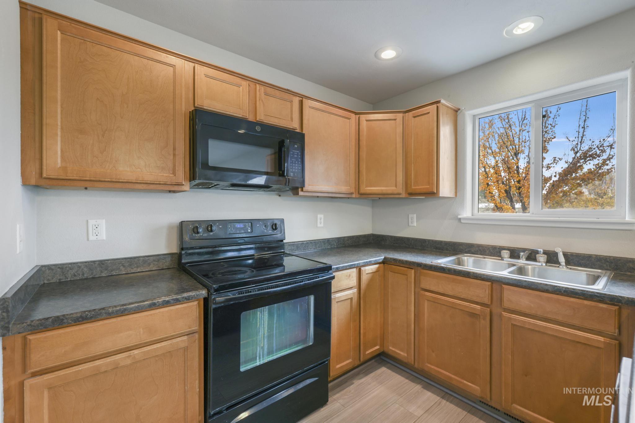 Kitchen featuring black appliances, dark countertops, brown cabinets, and recessed lighting