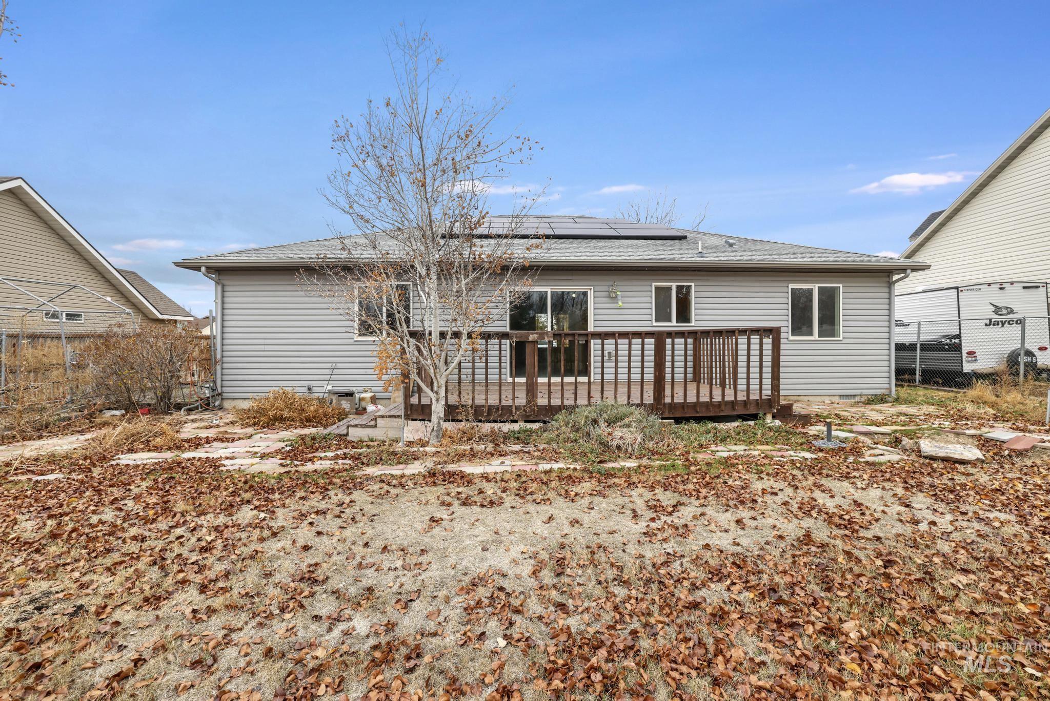 Back of property with a deck, roof mounted solar panels, and a shingled roof