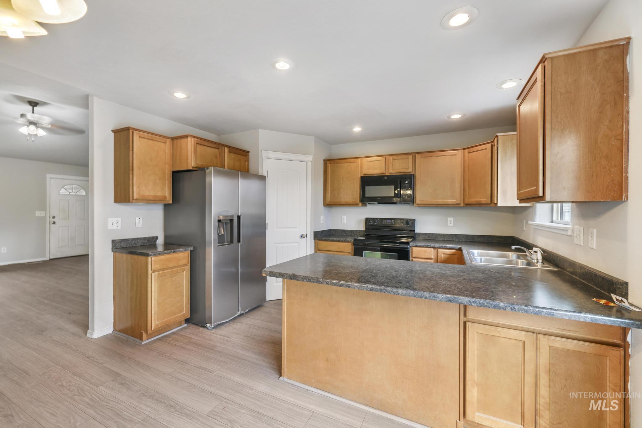 Kitchen featuring a peninsula, black appliances, light wood-type flooring, dark countertops, and recessed lighting