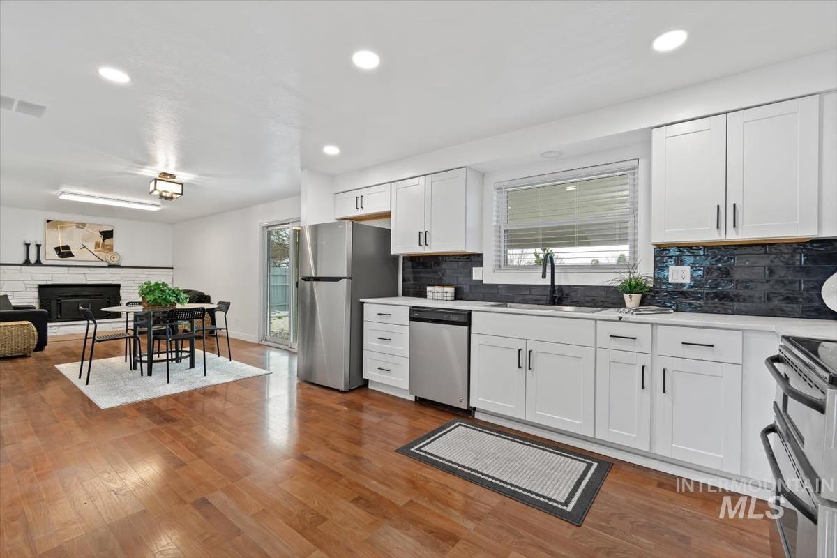 Kitchen with white cabinets, light wood finished floors, stainless steel appliances, recessed lighting, and a fireplace